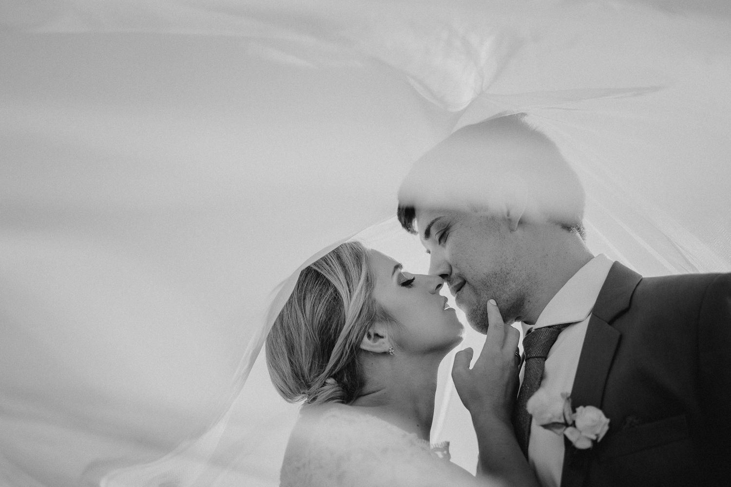 Black and white intimate wedding portrait with flowing veil creating ethereal effect.