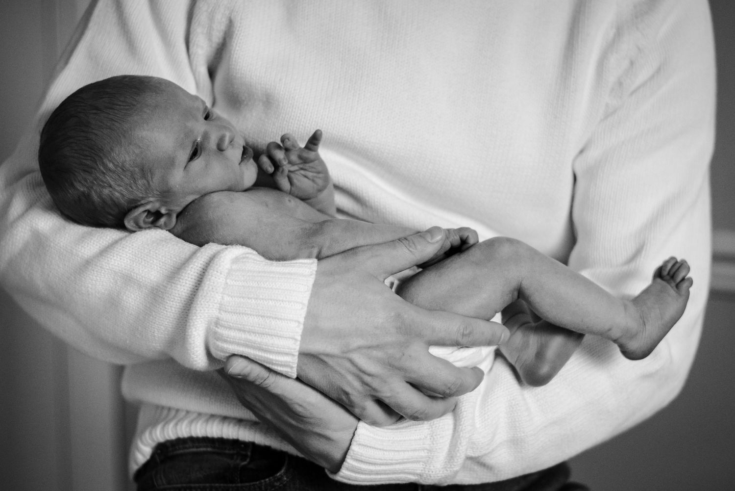 Black and White portrait of dad's strong arms holding a tiny newborn baby.