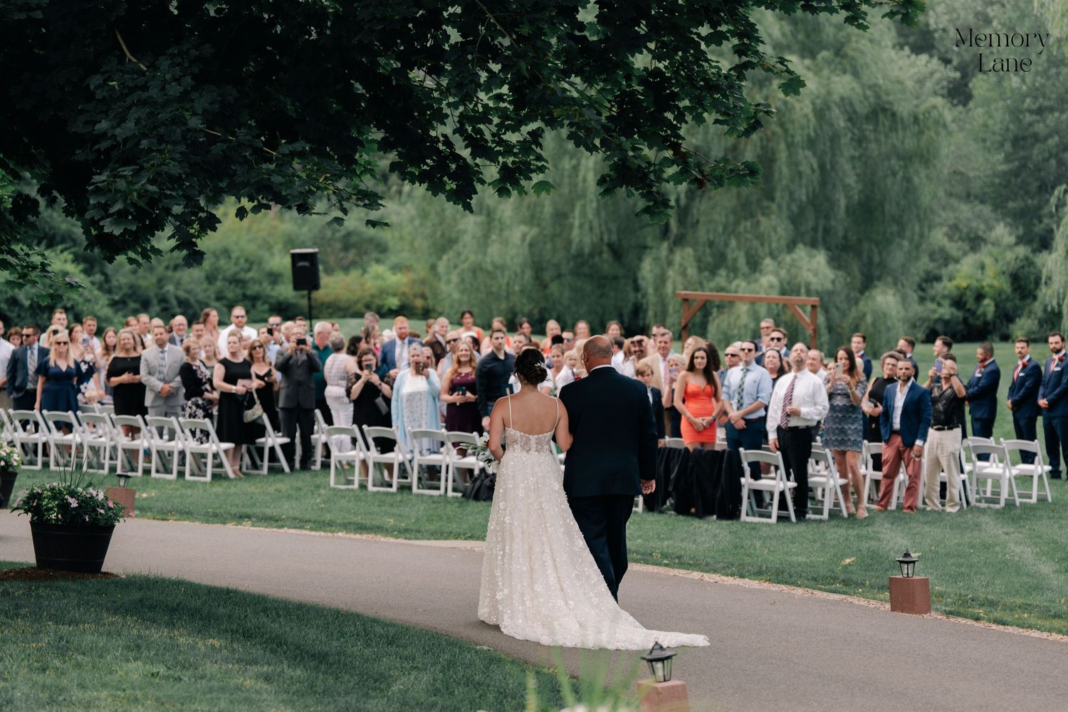 Wedding ceremony setup with white chairs on a lush green lawn filled with guests.