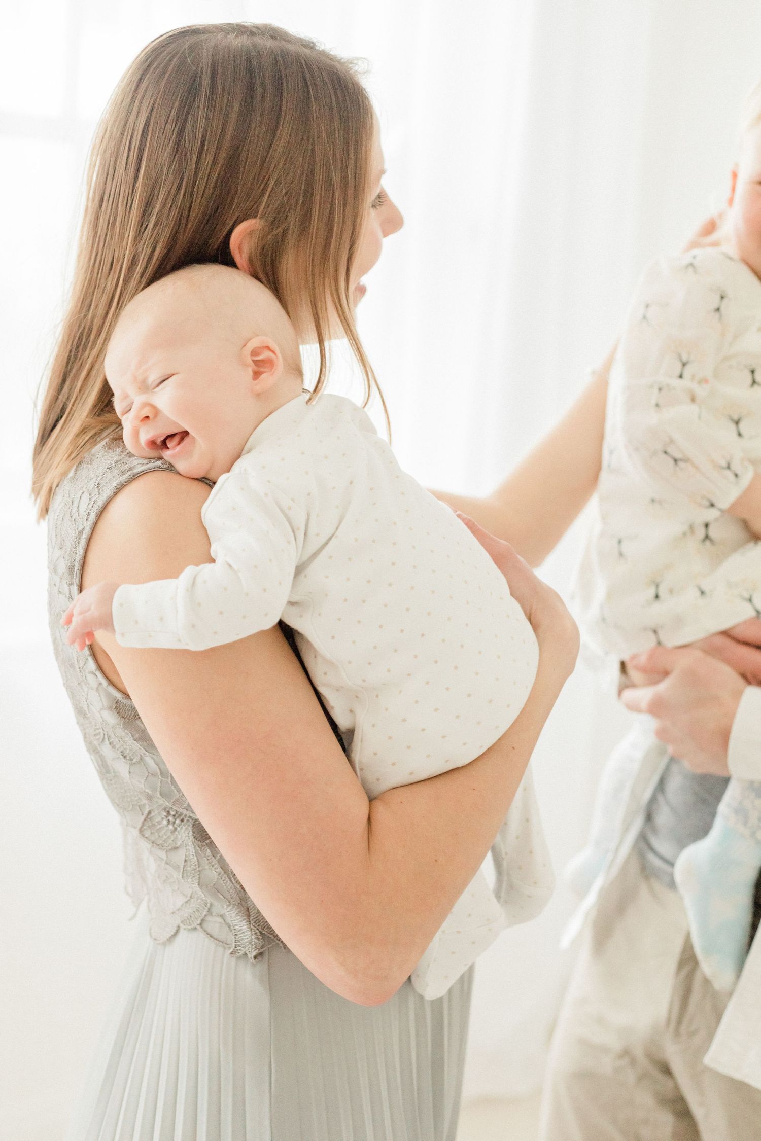 A tender moment captured in soft light shows a parent holding and comforting a small baby in white clothing.