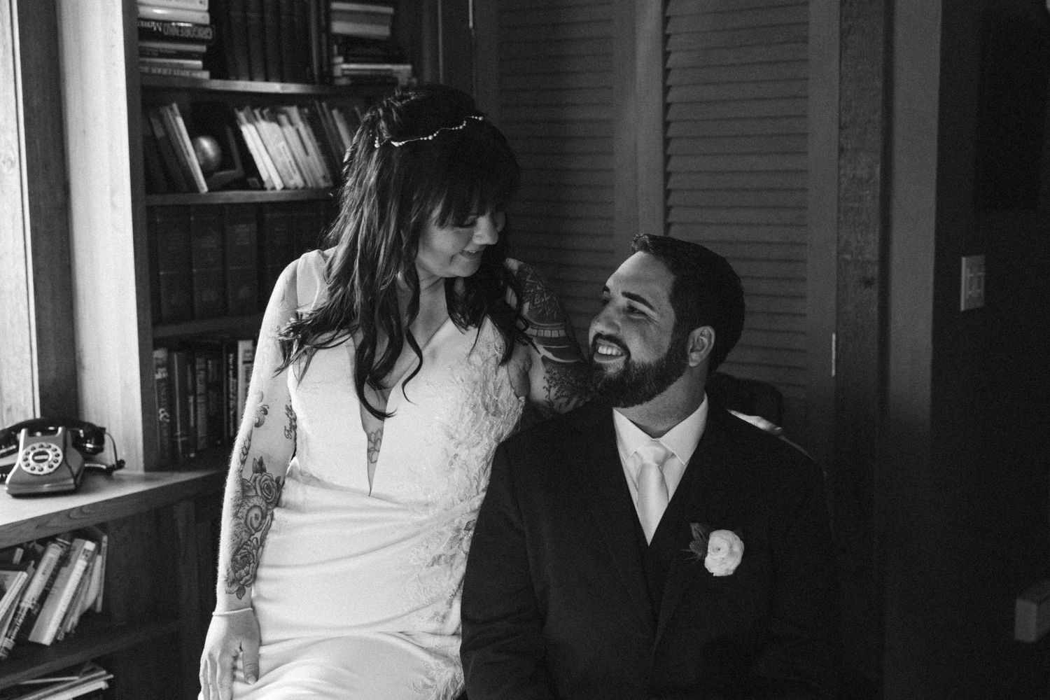 Black and white candid moment of couple laughing together in library setting.