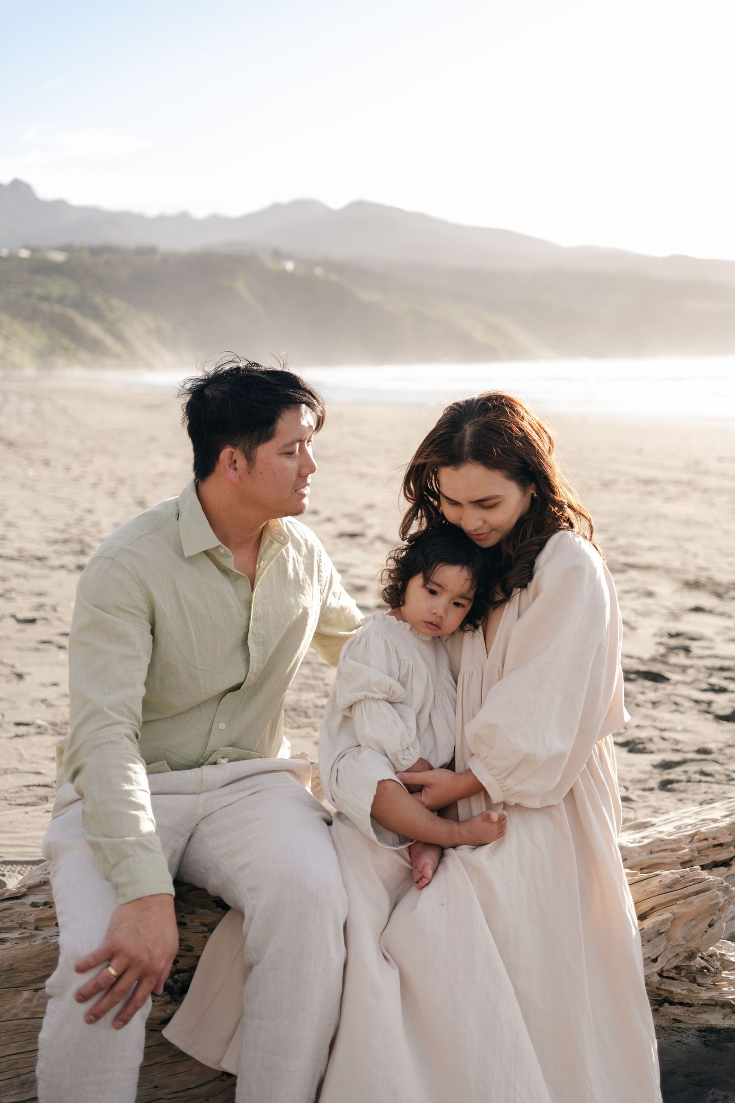 A tender family moment captured on a misty beach with neutral-toned clothing.