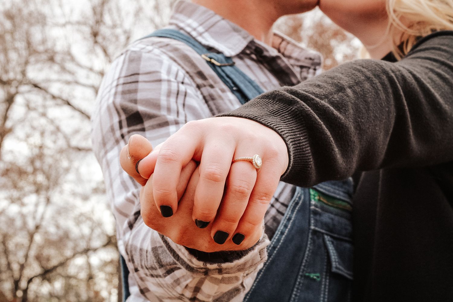 Close up of hands holding together with an engagement ring in a rustic outdoor setting.
