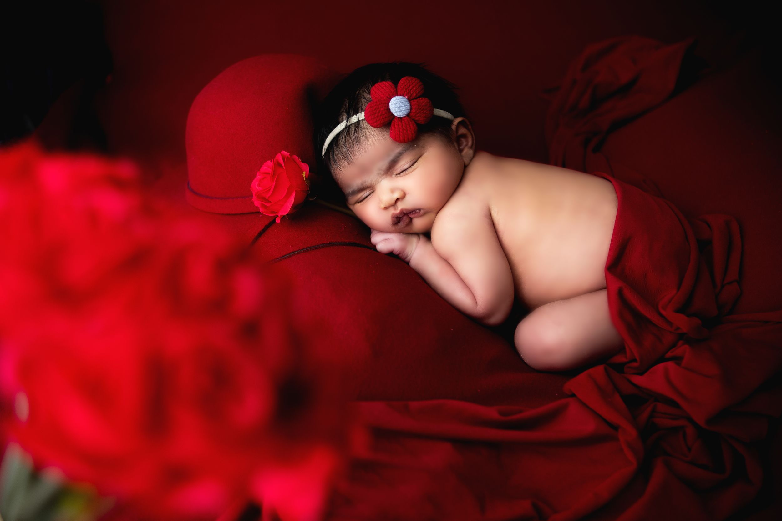 new born baby sleeping on red bed - Jasmeet K Photography