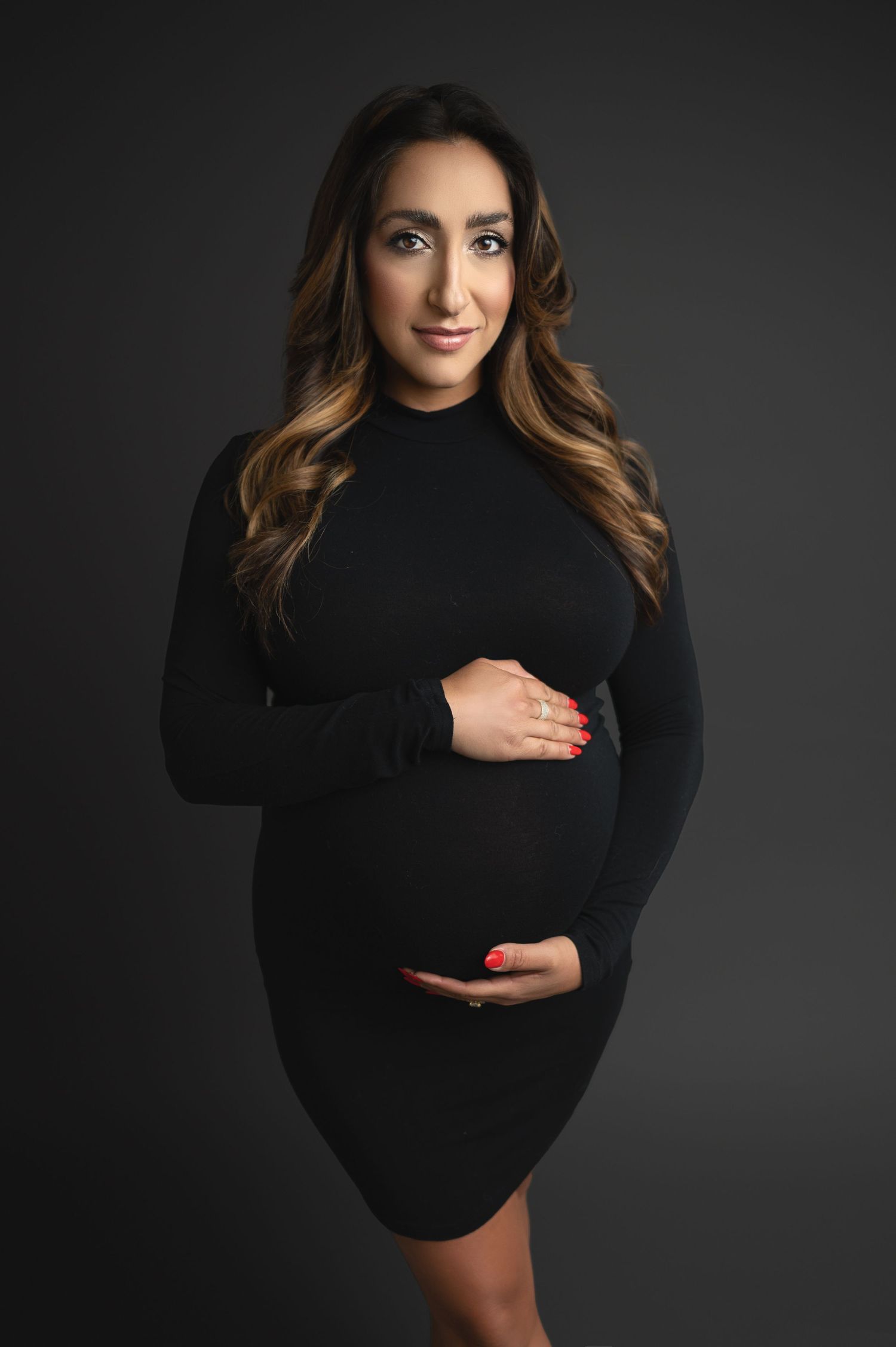 Studio maternity portrait with woman wearing black against dramatic lighting.