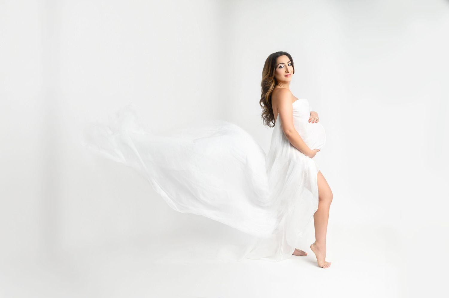 Artistic maternity photo of woman in white dress with fabric flowing in movement.