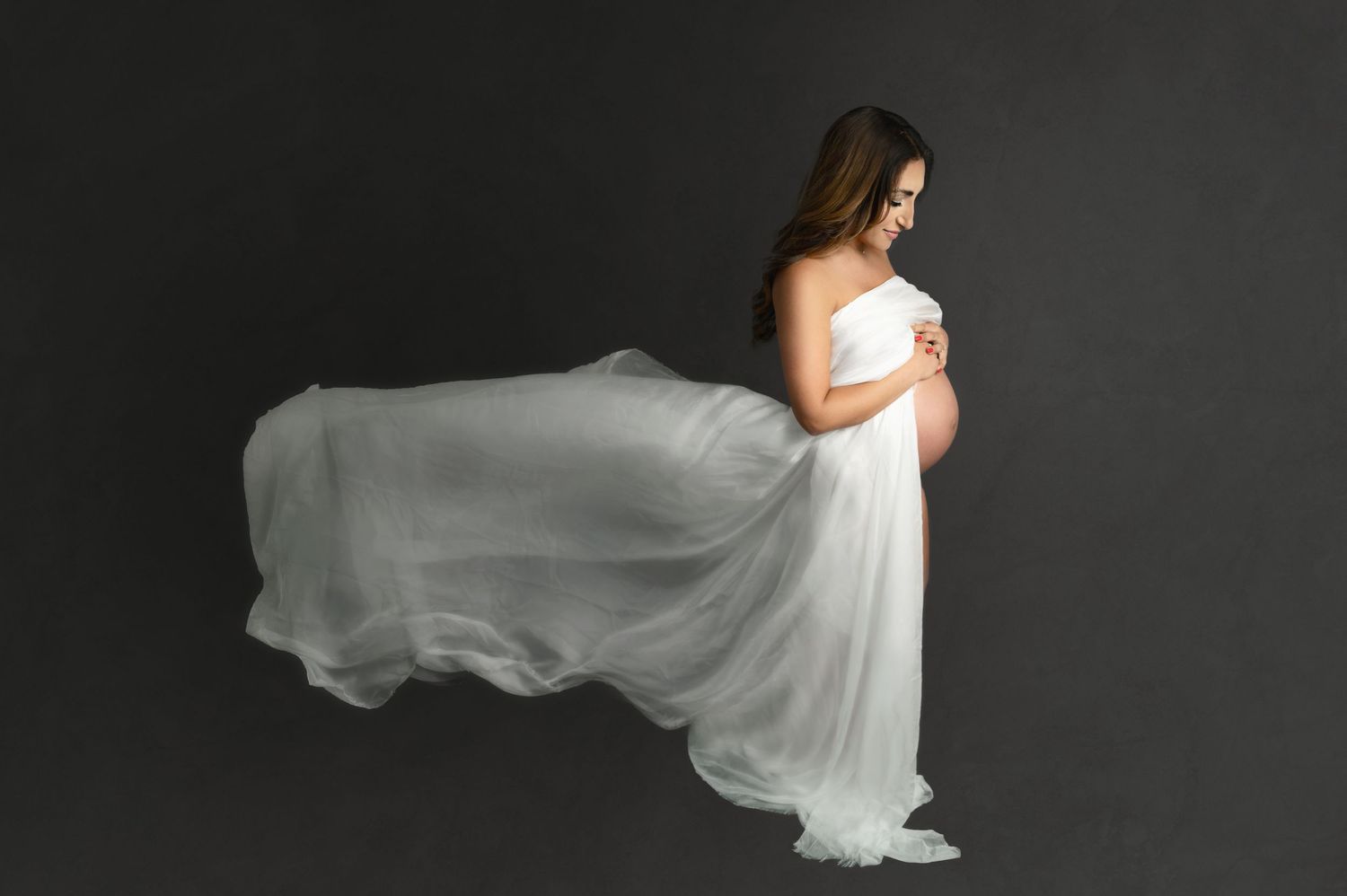 Dramatic maternity portrait with flowing white gown silhouetted against dark background.
