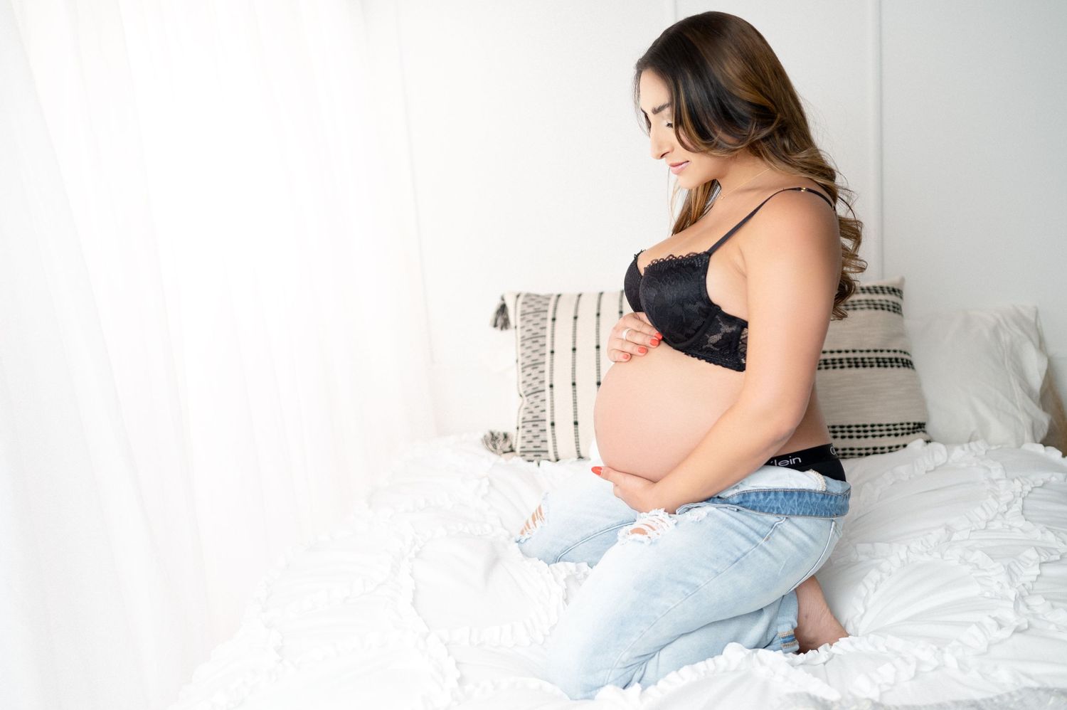 Casual maternity photo of expectant mother relaxing on bed with decorative pillows.