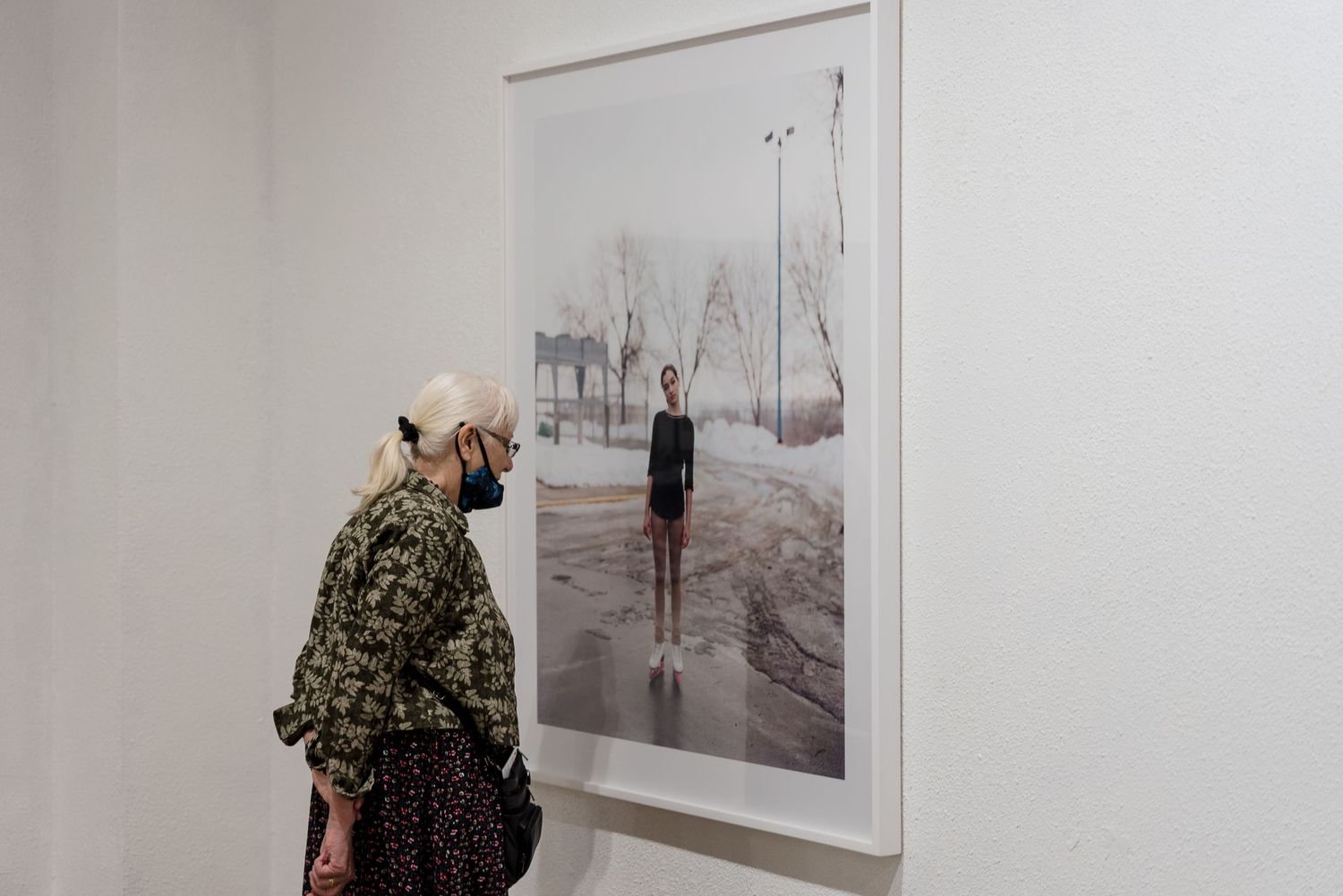 Gallery visitor observing black and white photograph in white-walled exhibition space.