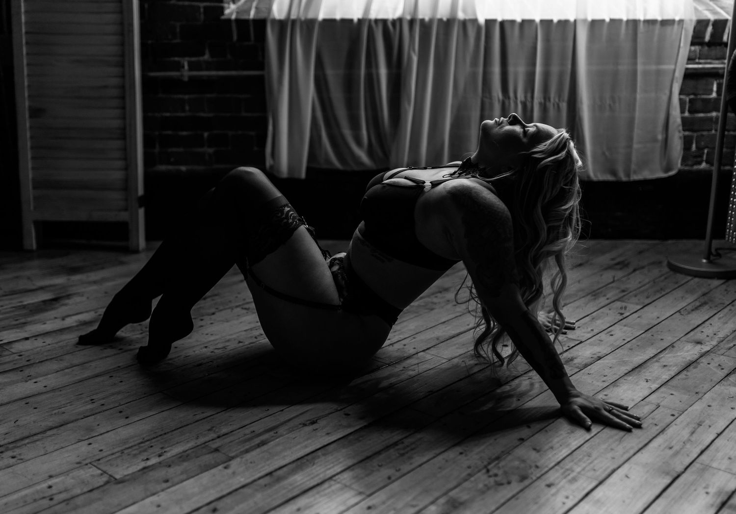 Artistic black and white boudoir photo on wooden floor with natural lighting.