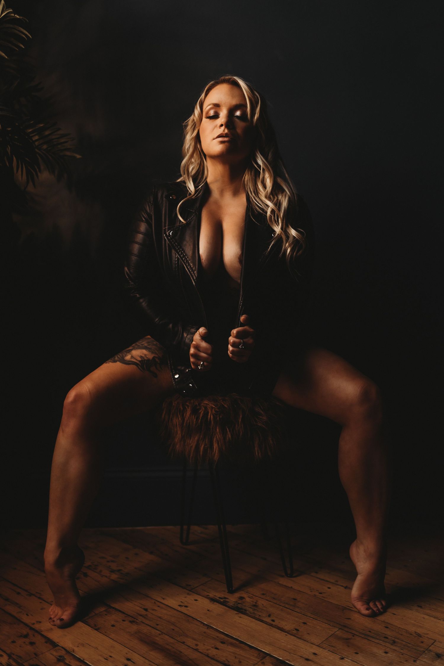 Moody boudoir portrait in dark setting showing person seated on wooden chair with dramatic lighting and shadows.