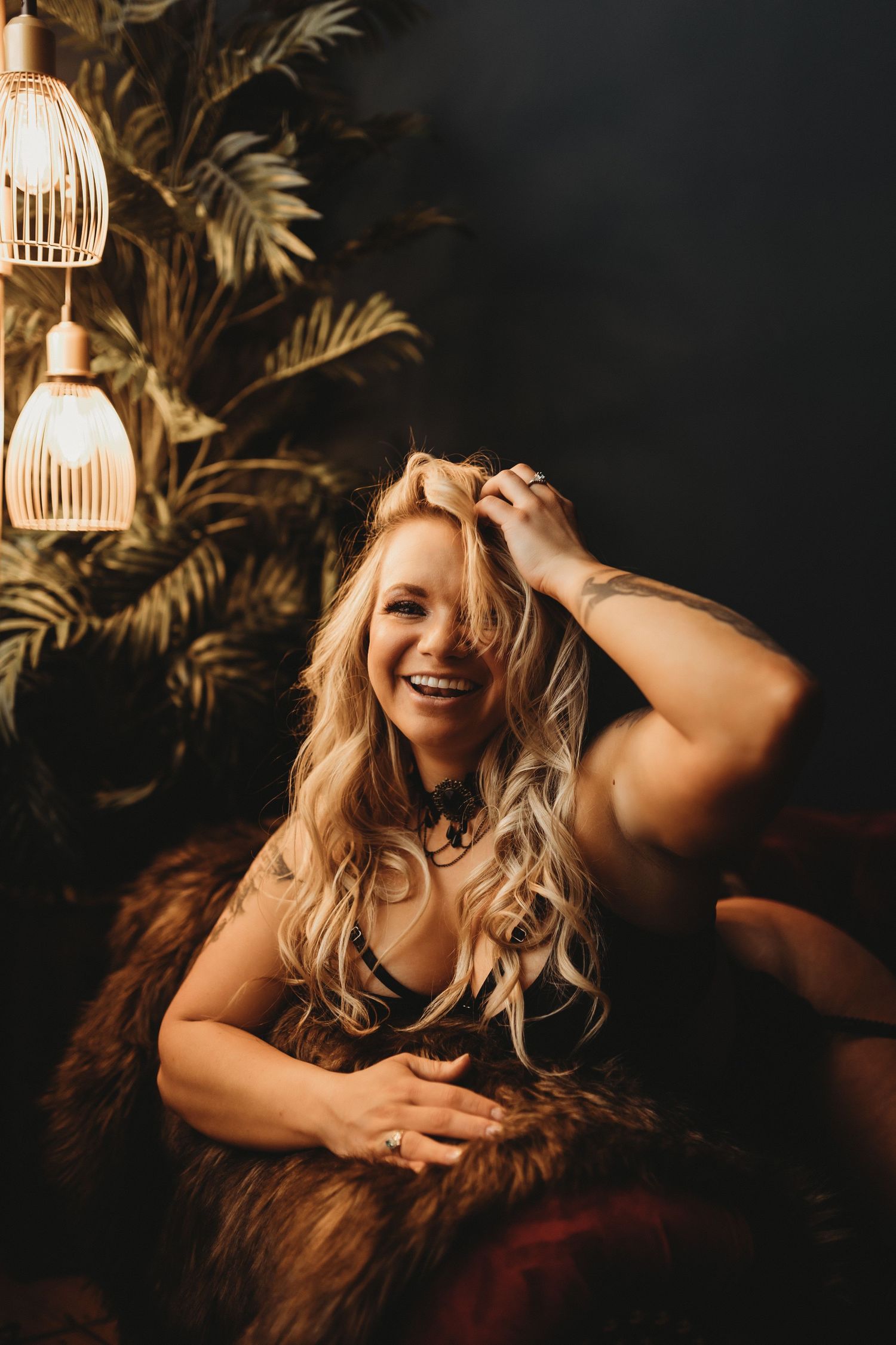 Intimate boudoir portrait with decorative lighting and tropical plants in background.