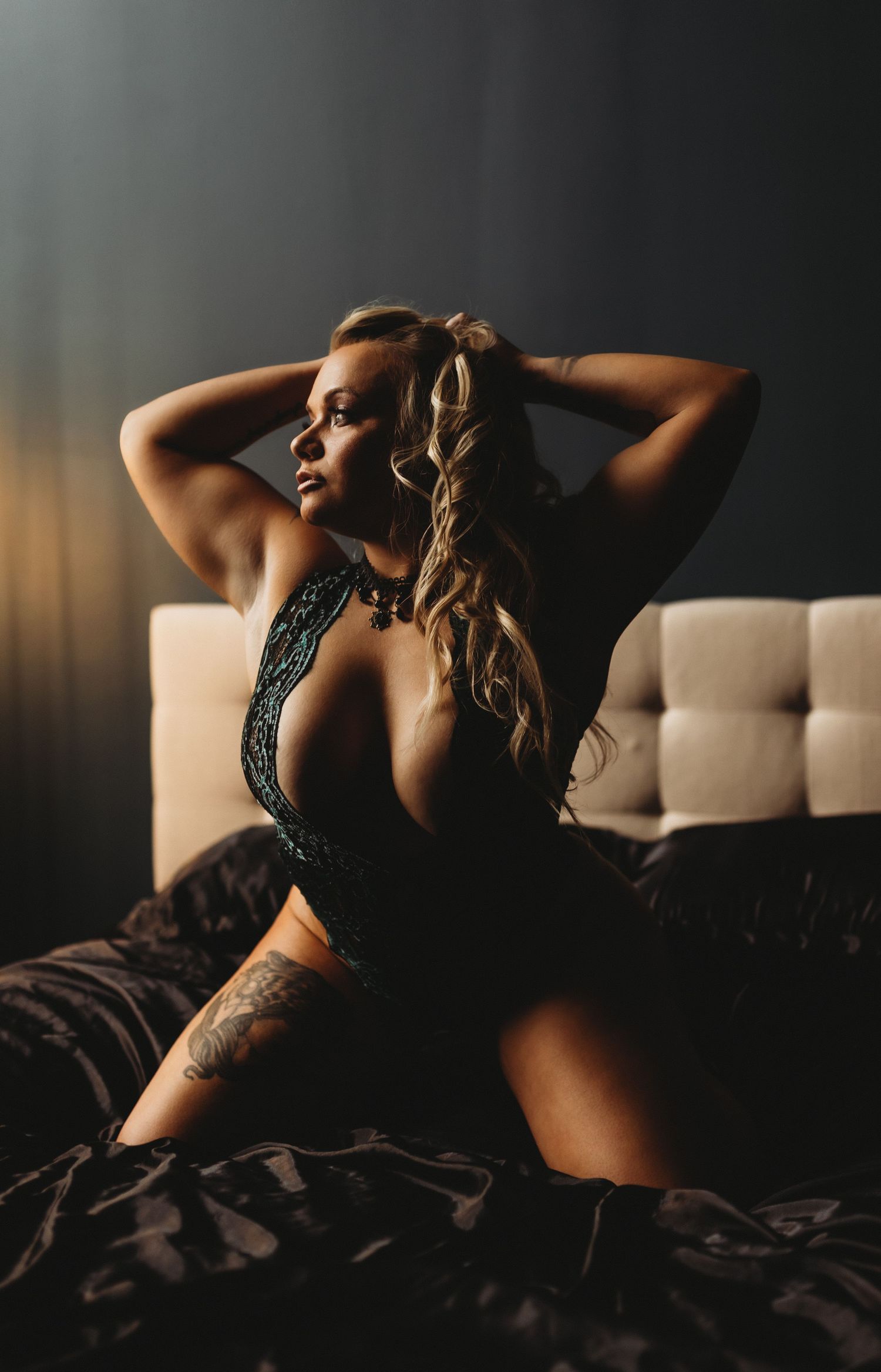 Silhouette of figure in black lace lingerie poses sensually on tufted couch in moody lighting.