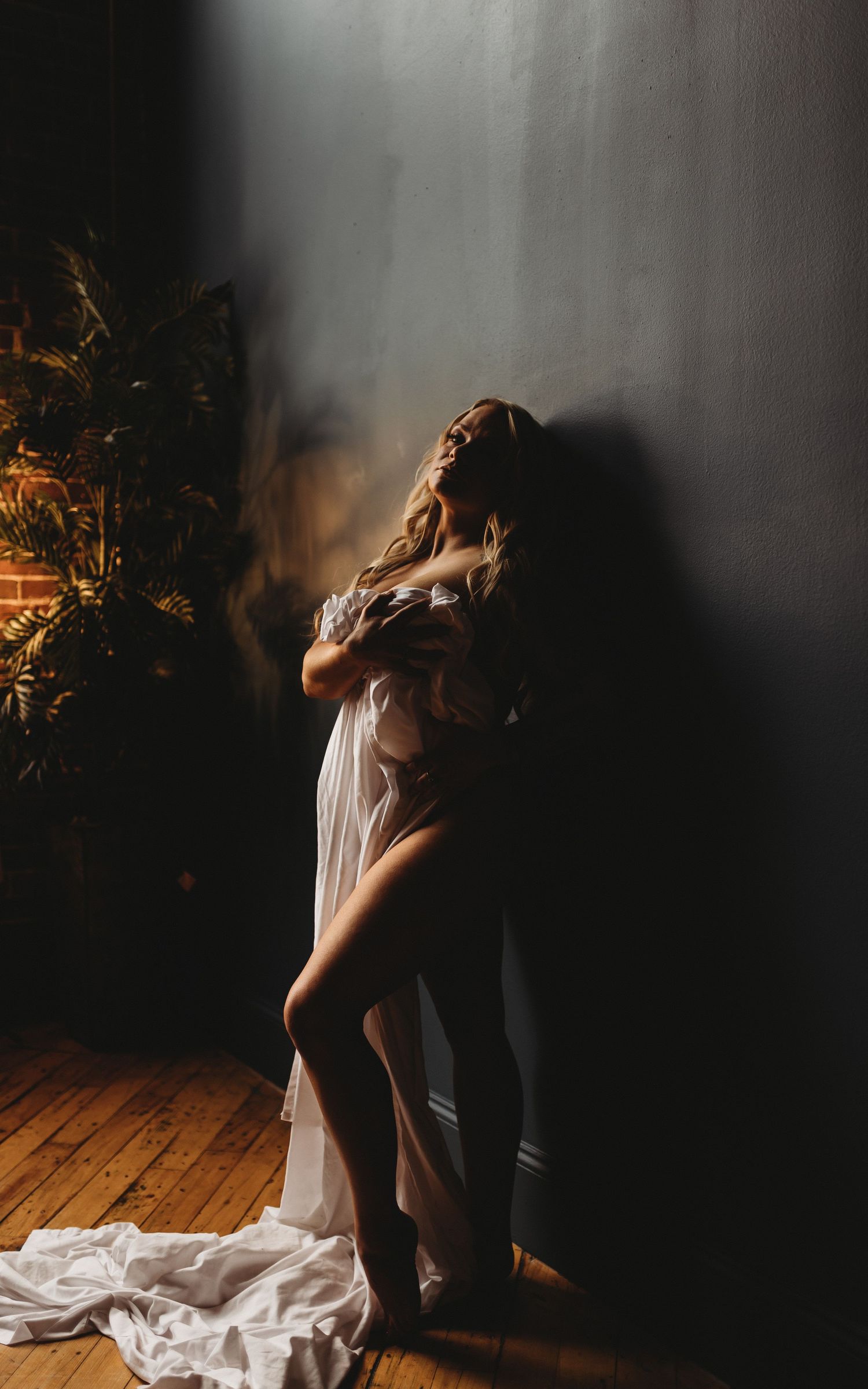 Artistic portrait with dramatic lighting against brick wall and flowing white fabric.