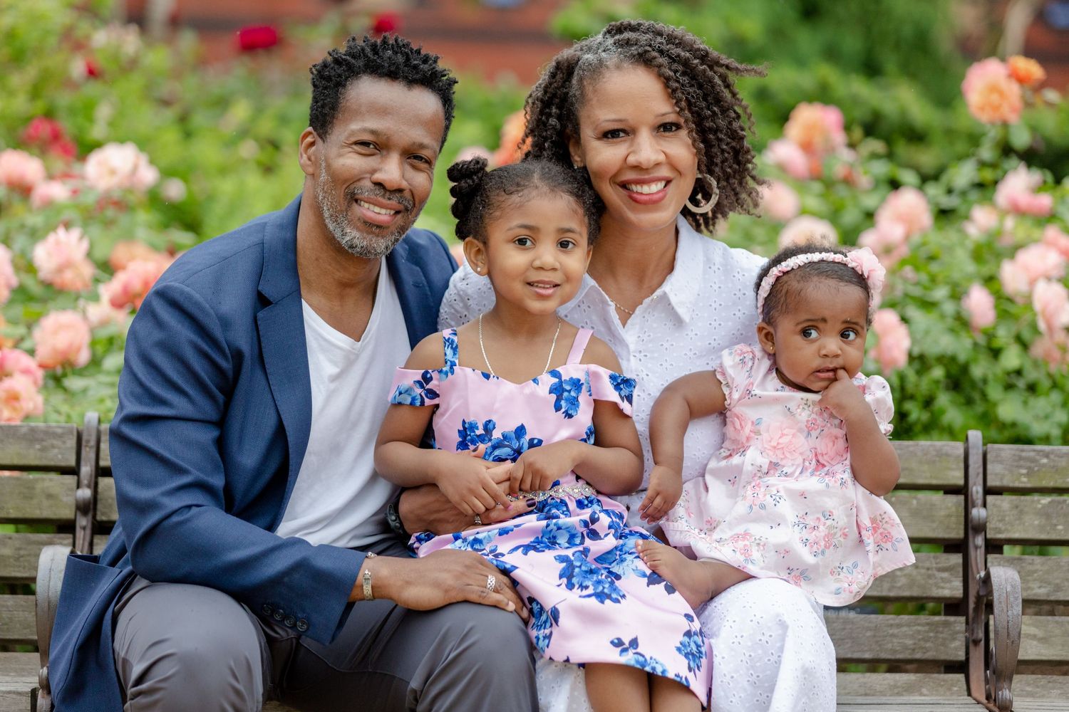 Family of four smiling together on a park bench surrounded by flowers.