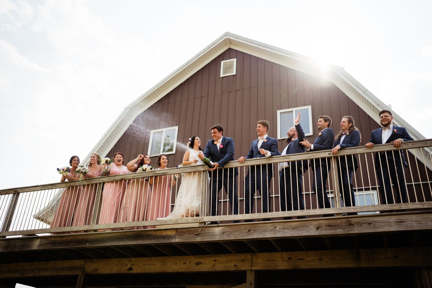 Wedding party poses on a rustic barn balcony during golden hour.