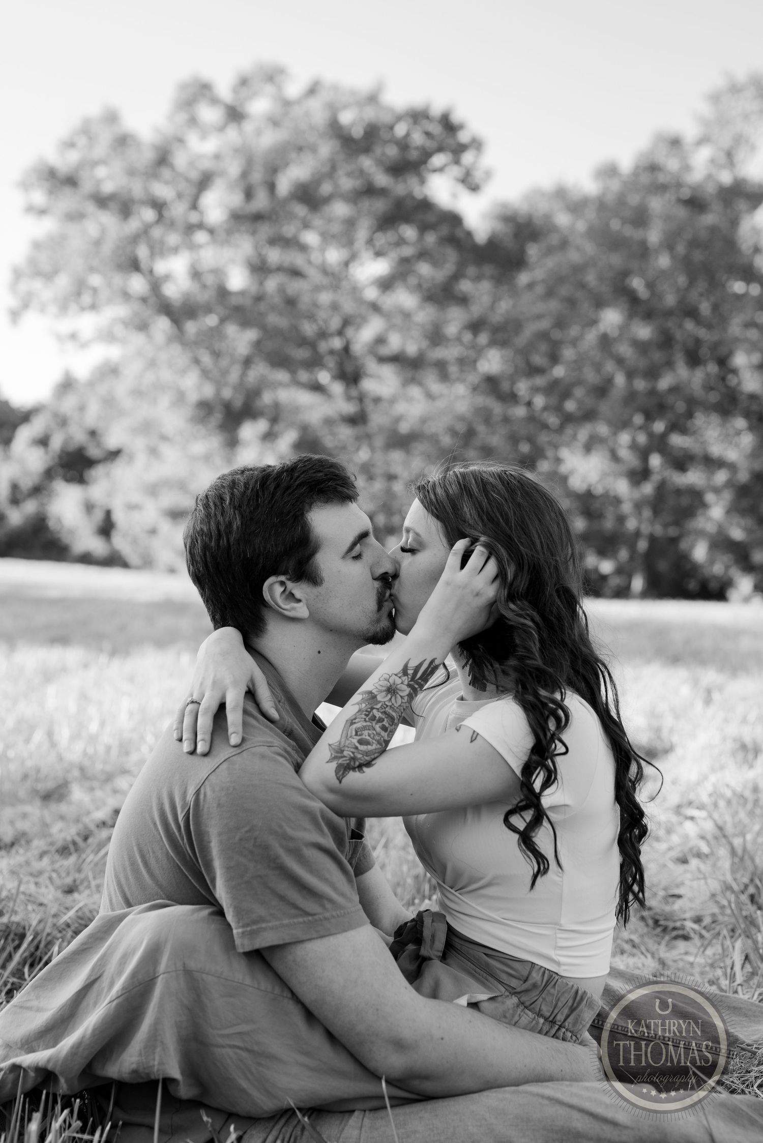 A romantic black and white portrait of a couple sharing an intimate moment in a field.