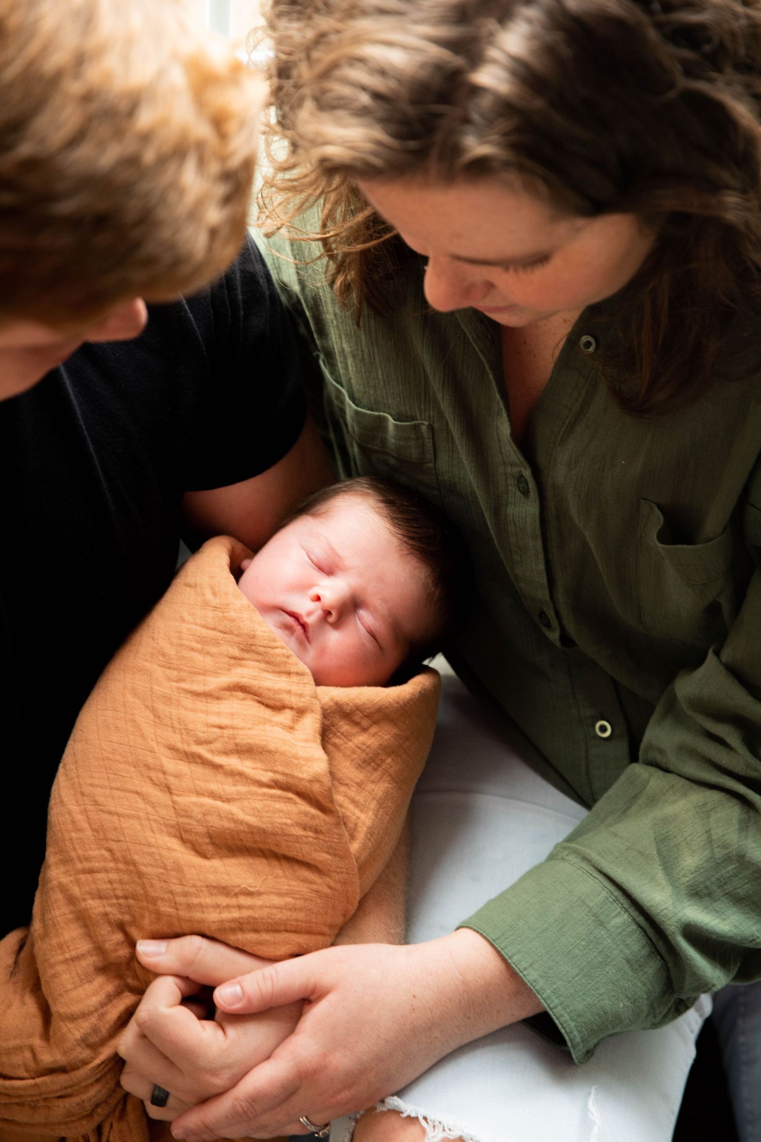 Gentle nurturing moment with newborn wrapped in orange blanket.