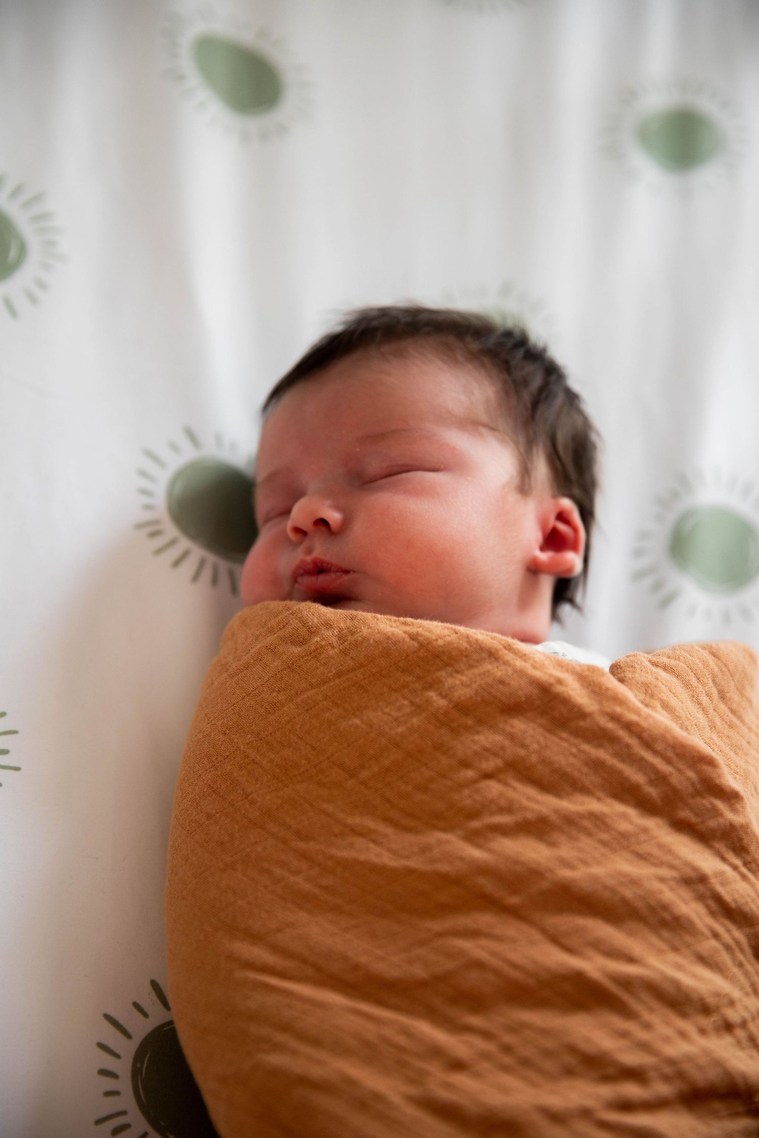 Sleeping newborn wrapped in soft orange swaddle against white background.