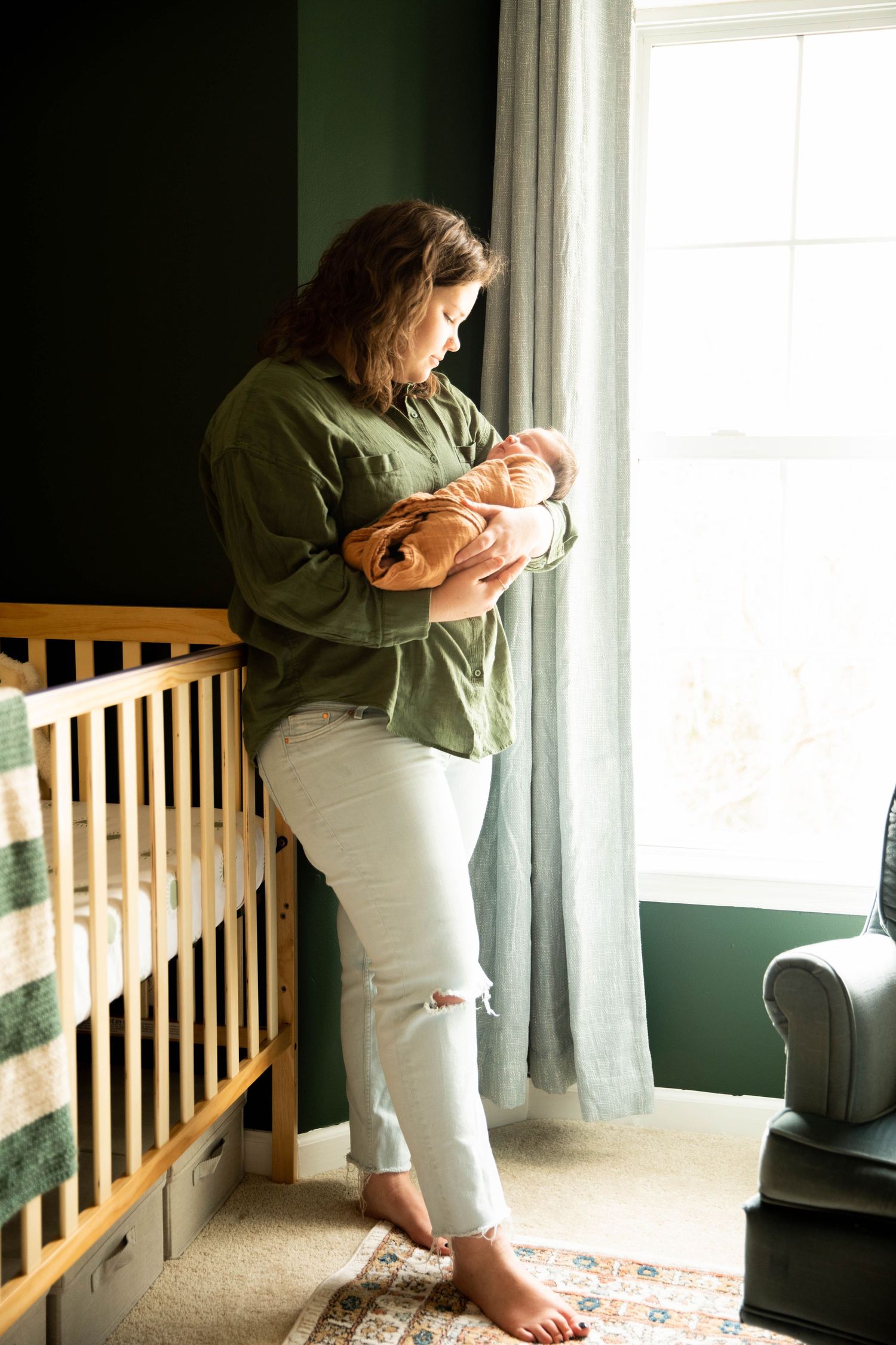 A tender moment by a window in a nursery with green walls and wooden crib.