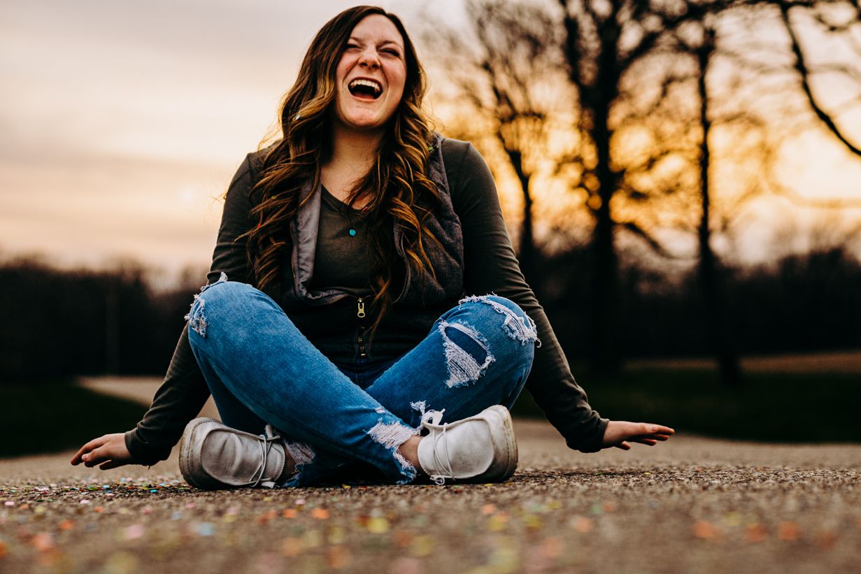 Person sitting cross-legged on fallen leaves during golden hour sunset.