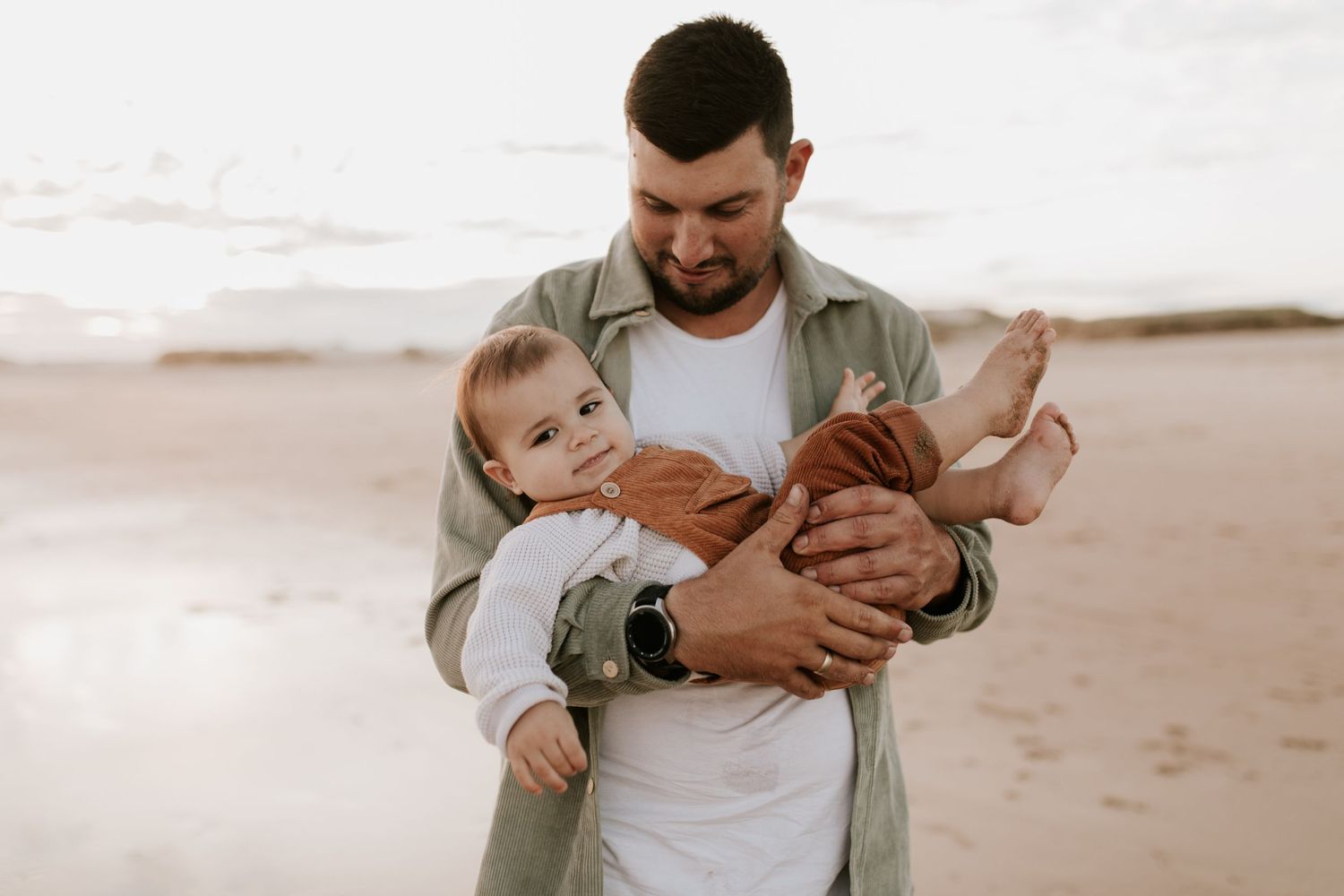 A parent holding a small child on a sandy beach at sunset.