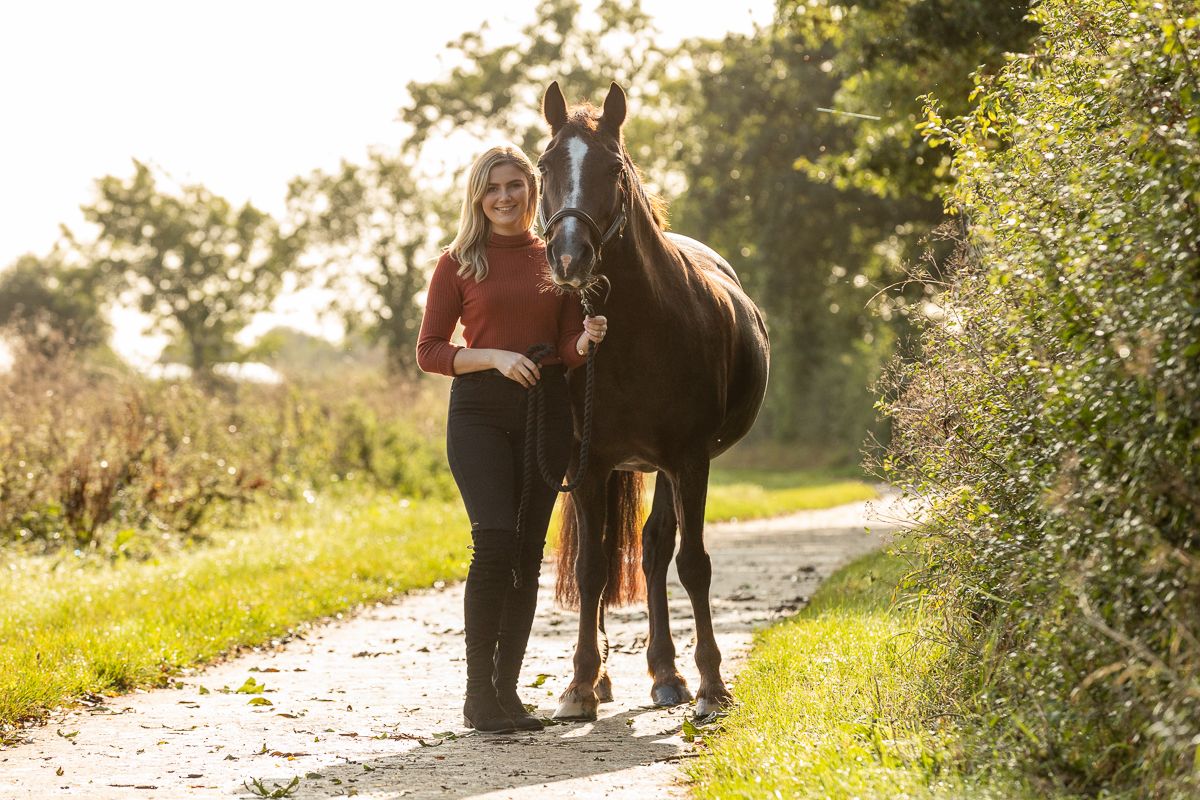 Casual portrait of equestrian with bay horse on countryside trail at sunset.