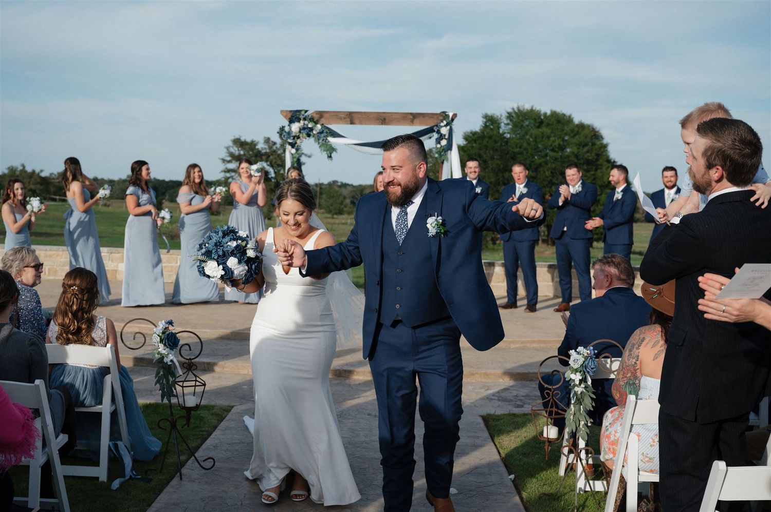 A celebratory recessional at an outdoor wedding ceremony with guests looking on.