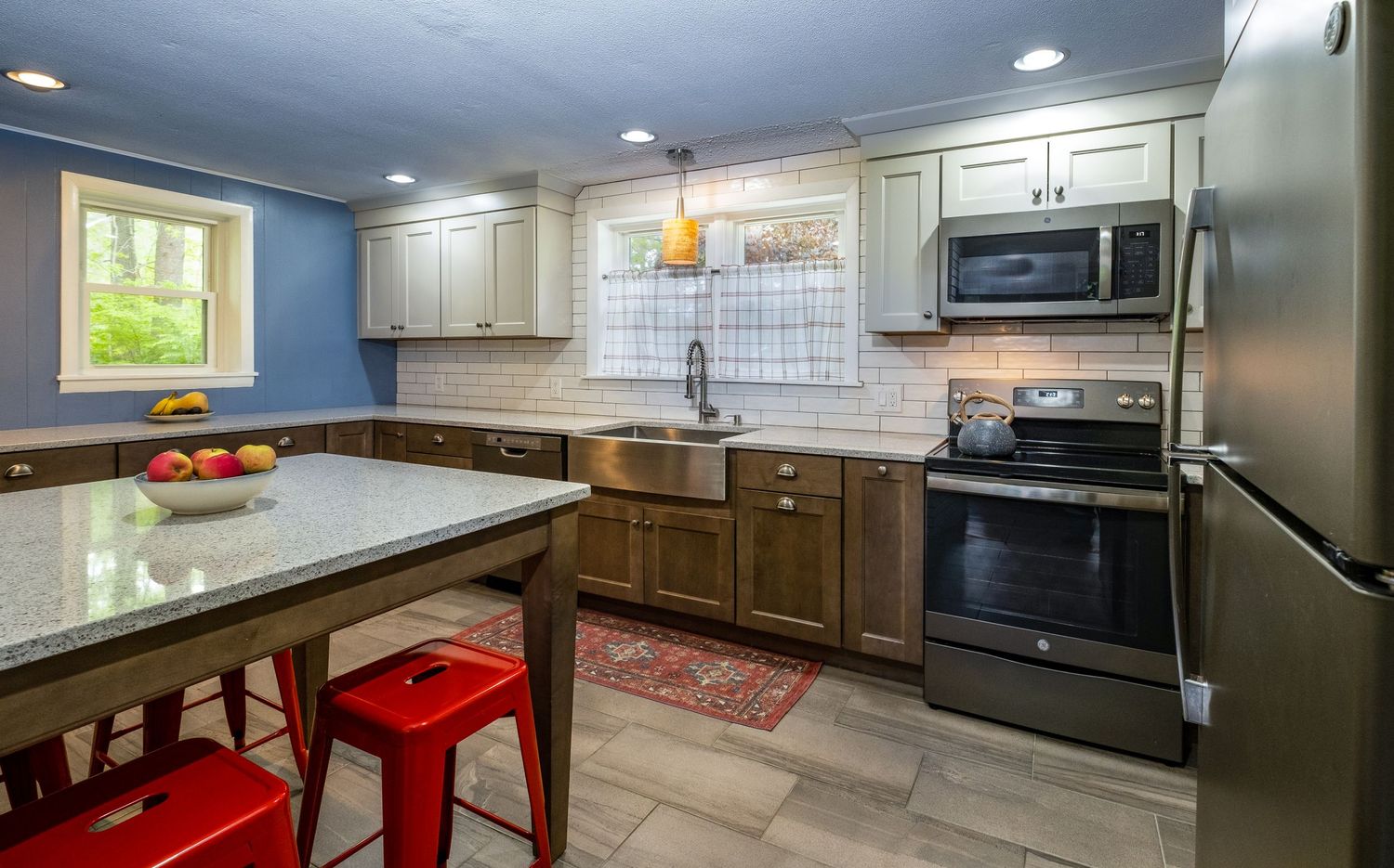 Contemporary kitchen with two-tone cabinets, tile backsplash, and red metal stools.
