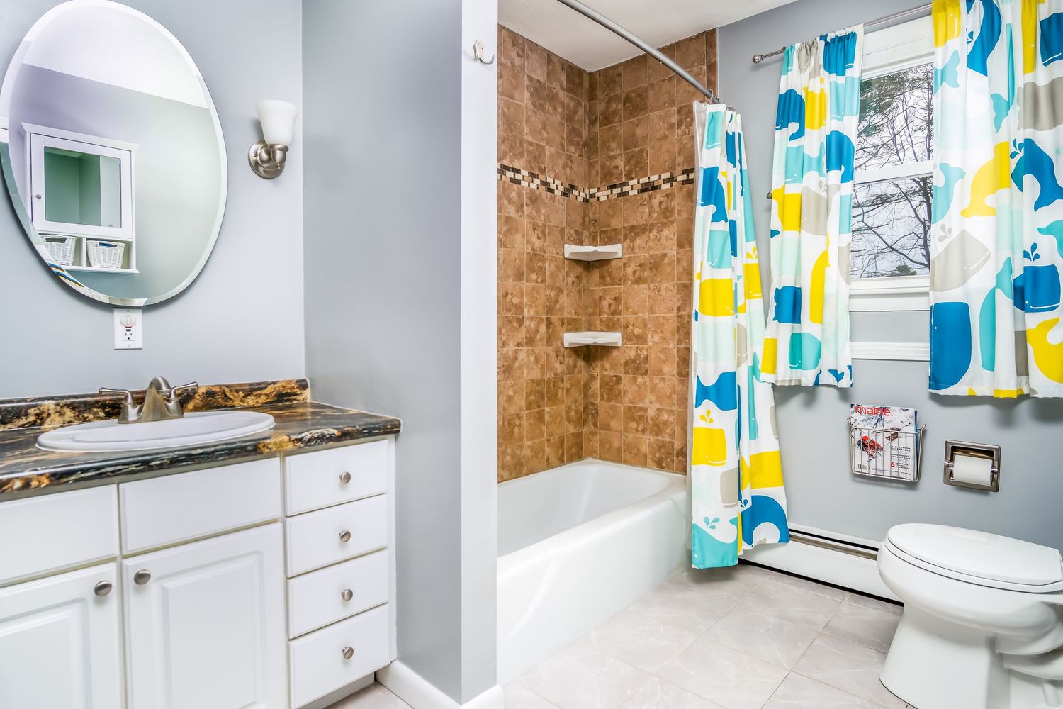 Modern bathroom with white vanity, round mirror, and colorful blue and yellow shower curtain.