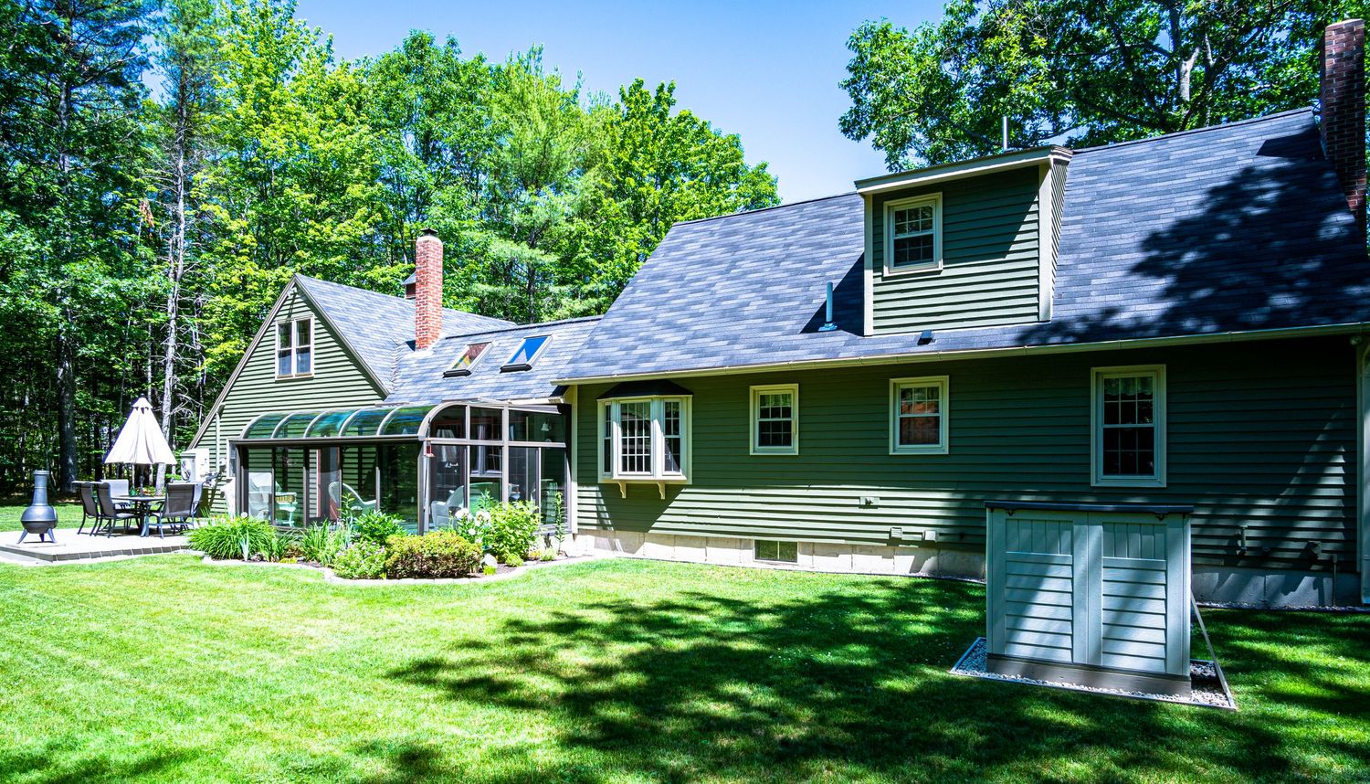 Green ranch-style house with dormers and well-maintained lawn surrounded by trees.