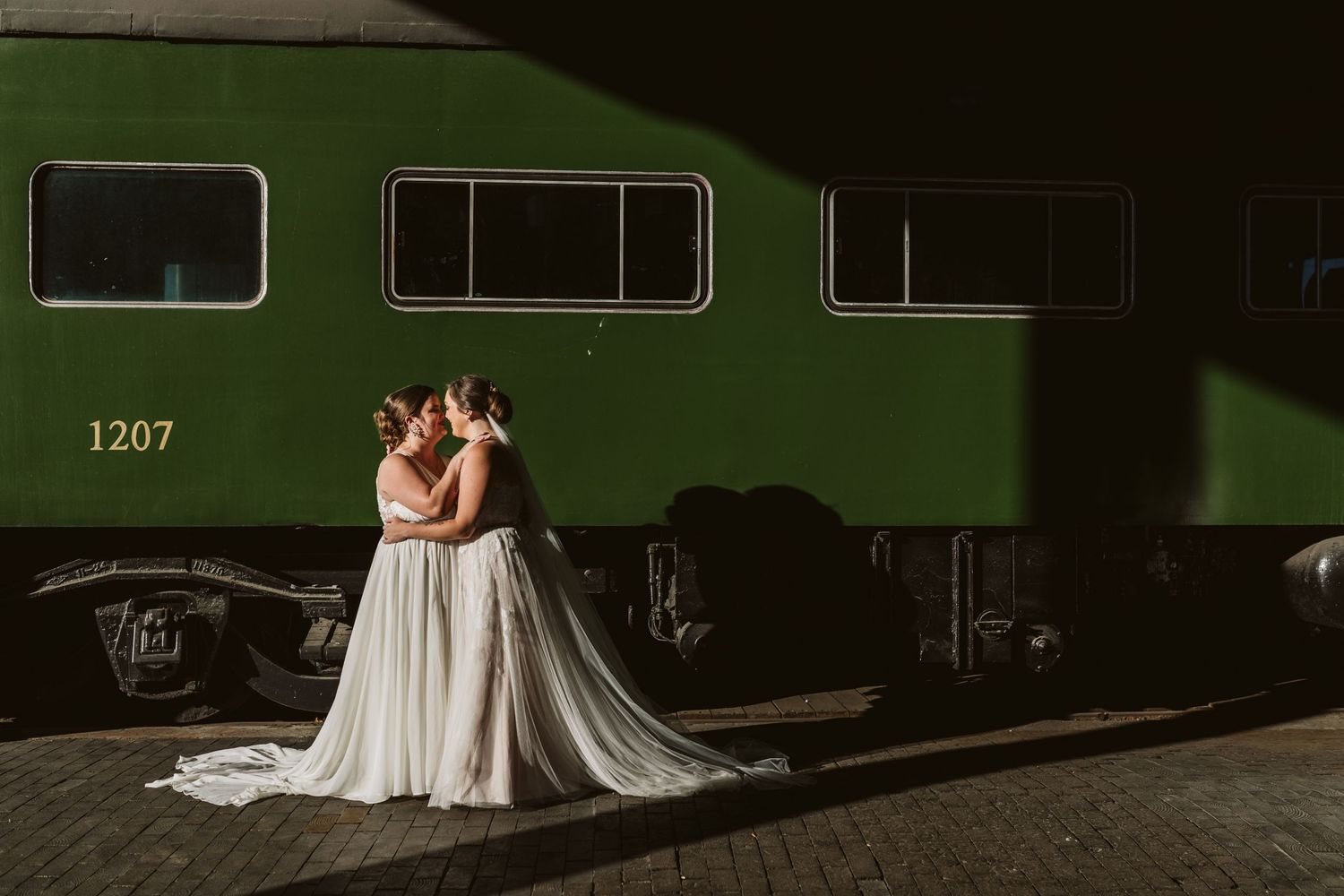 A couple poses dramatically next to a vintage green train car.