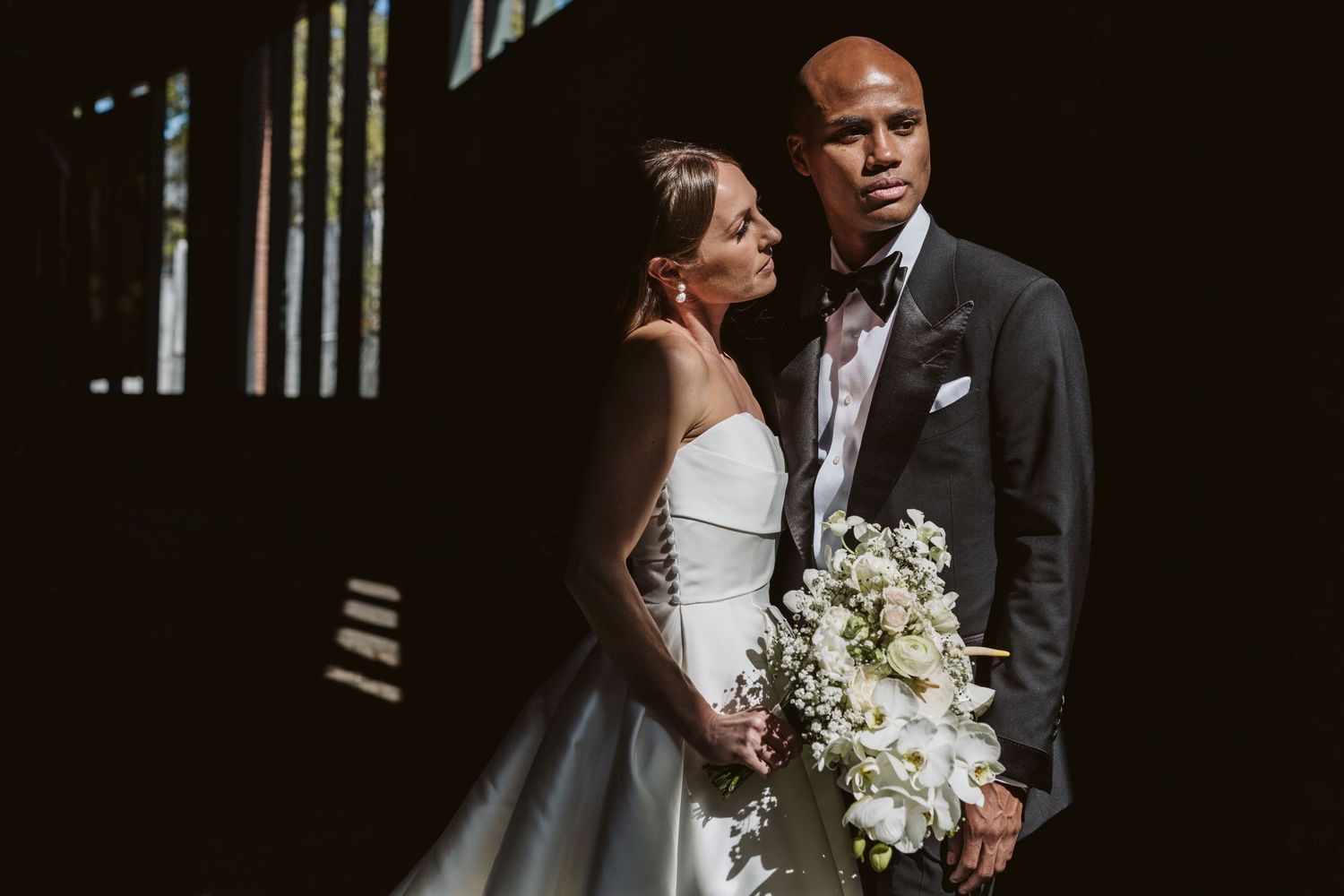 Elegant wedding portraits in dark setting with white floral bouquet.