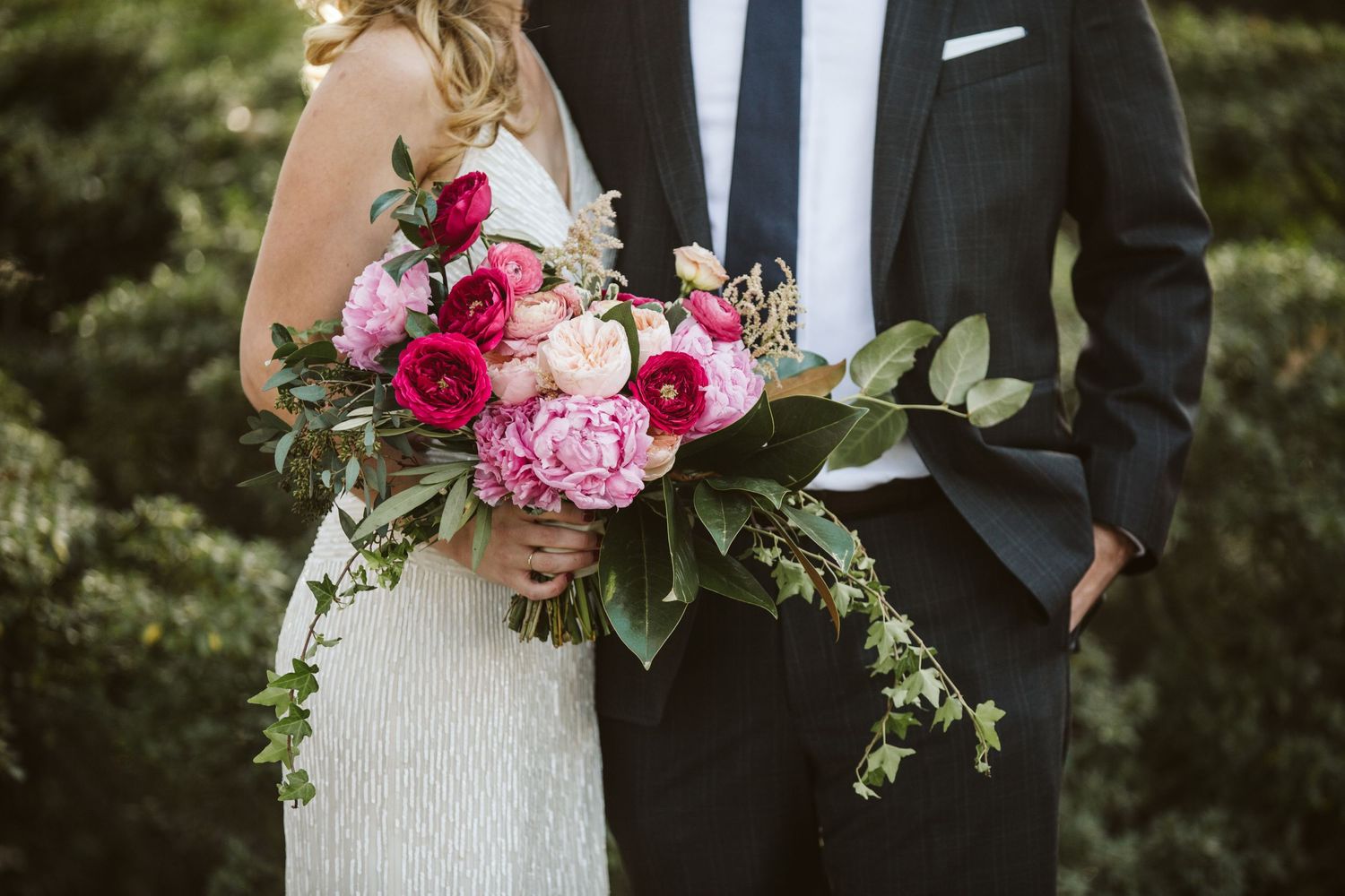 Elegant couple holding pink peony bouquet in formal wedding attire.