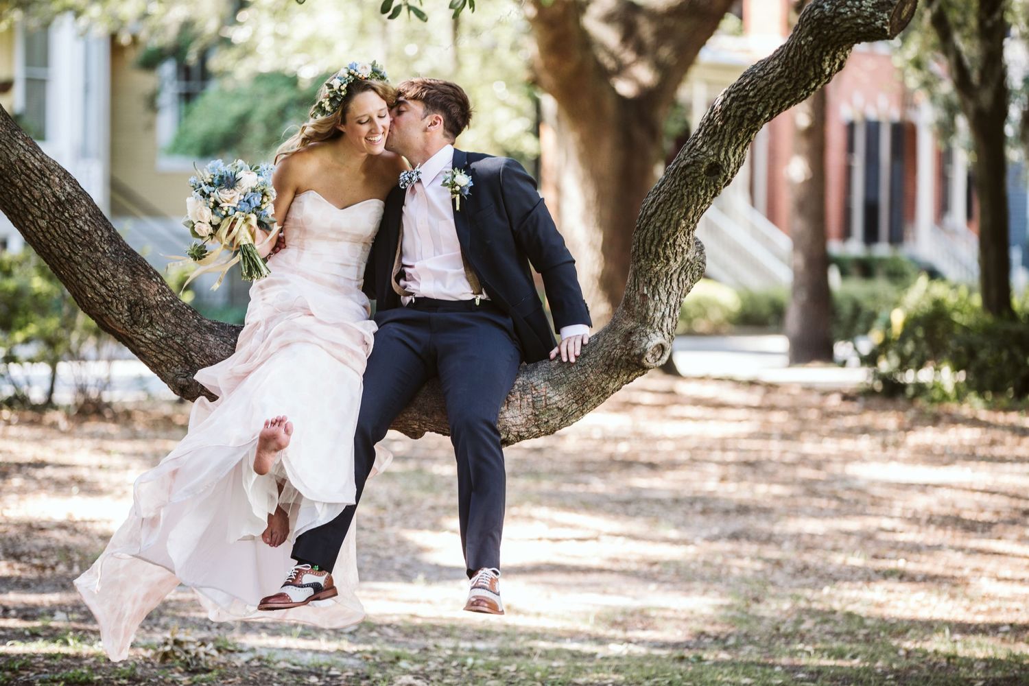 Romantic wedding couple poses under a large tree with dappled sunlight.