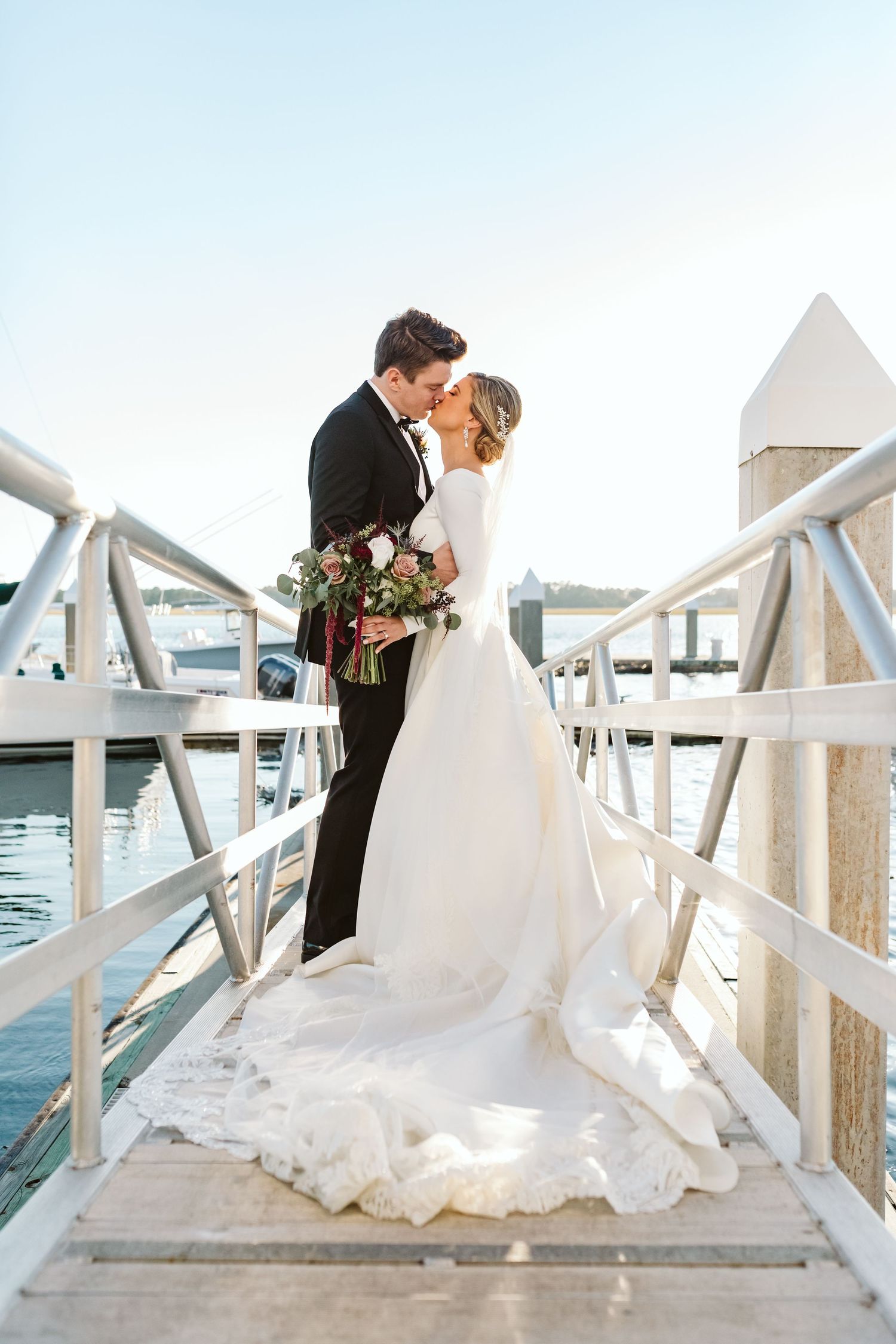 A couple shares romantic moments on a white wooden dock by the water.
