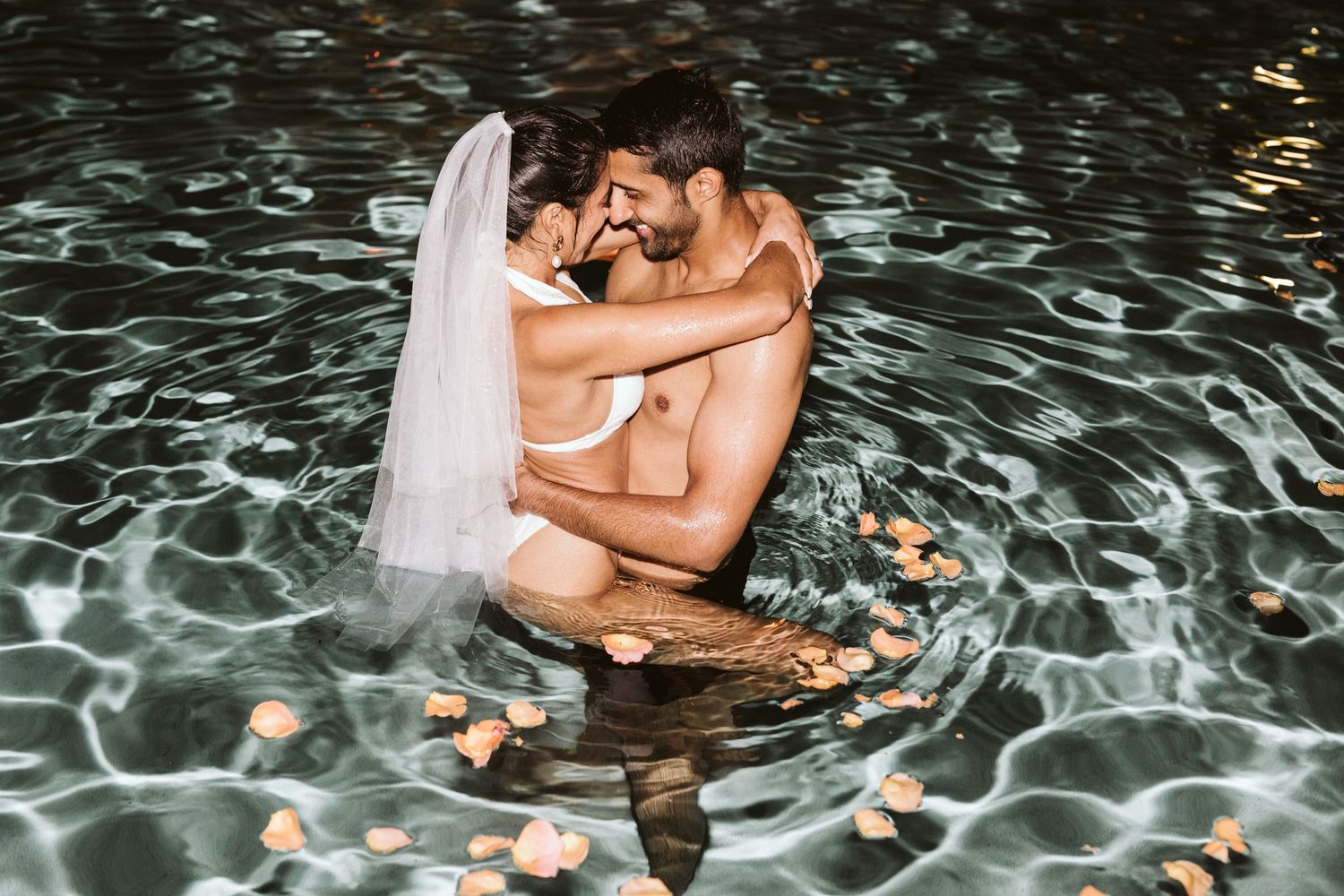Artistic water photography series of couple embracing in pool with floating flowers.