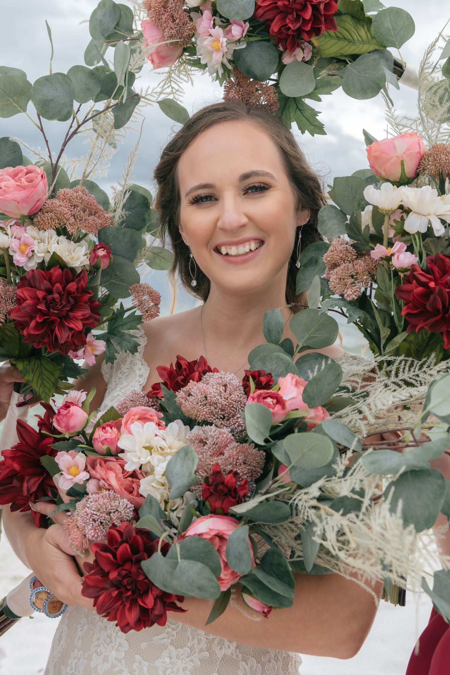 Wedding bouquet with deep red dahlias, pink roses, and eucalyptus framing portrait.