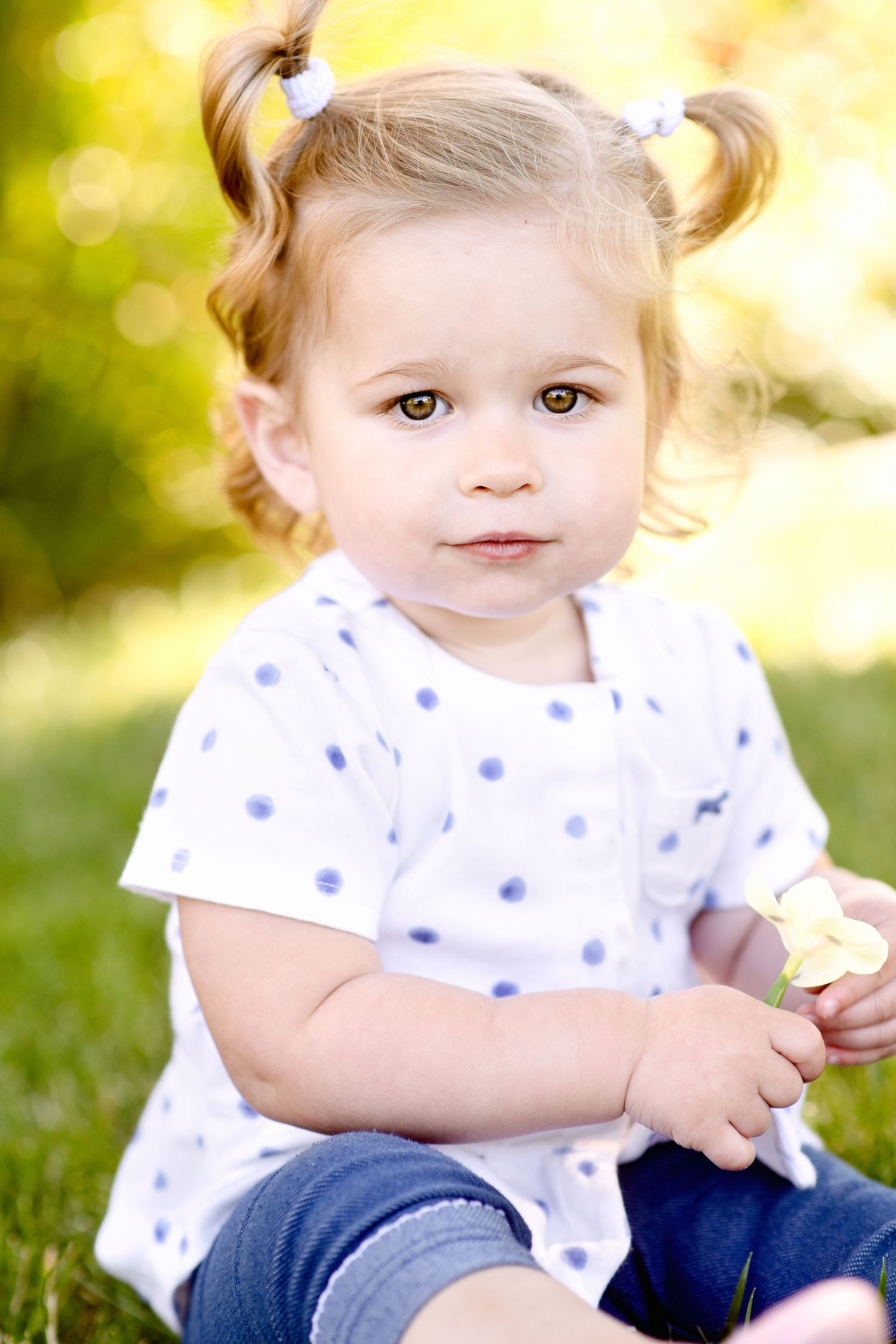 Toddler with pigtails wearing polka dot dress sitting in grass.