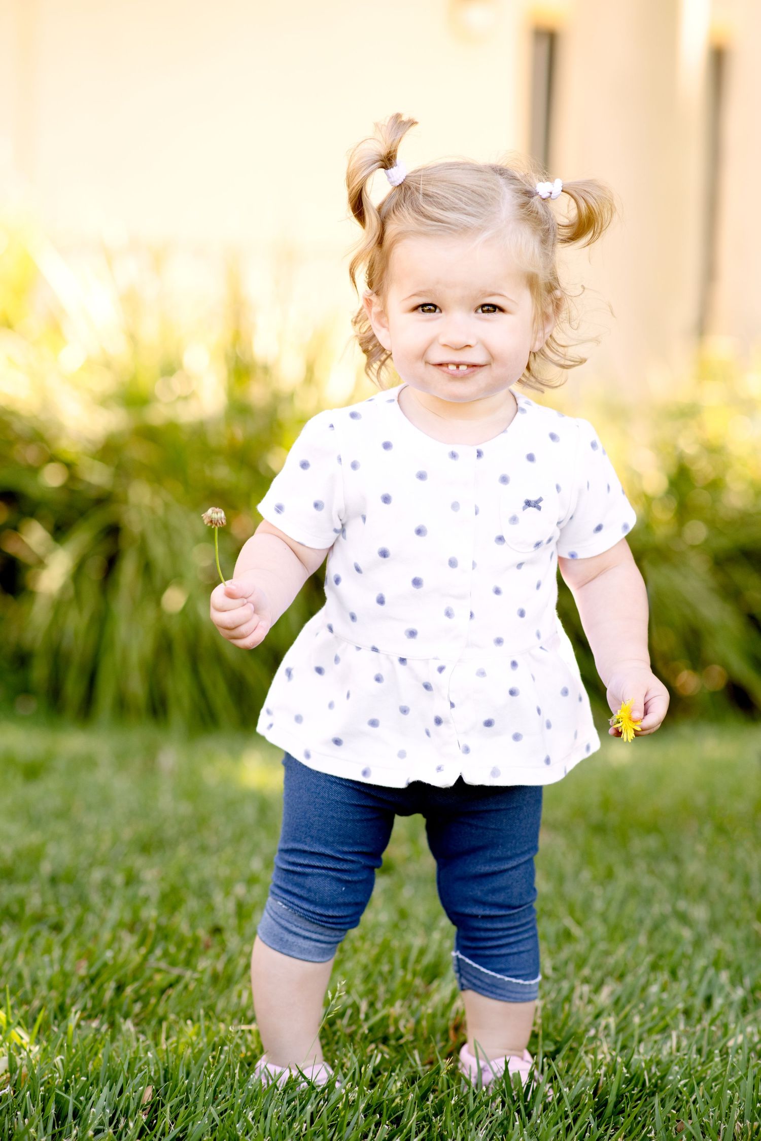 Toddler in white polka dot top playing on grass during golden hour photo session.