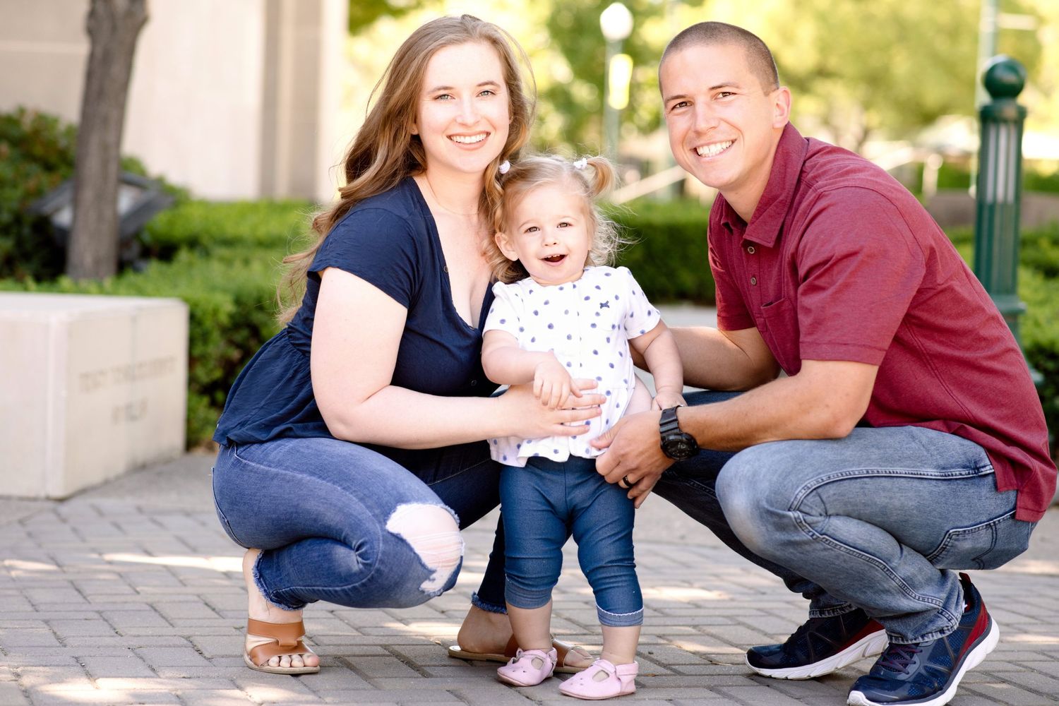 A family poses together while crouching on paved ground with a building in the background.