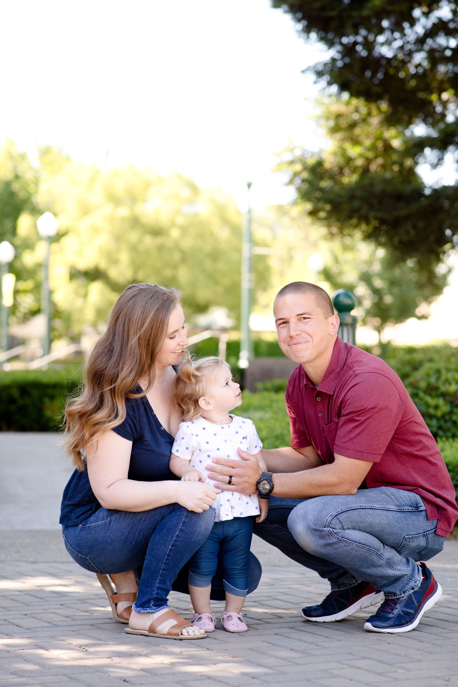 A family crouches together on a brick pathway surrounded by landscaping and trees.