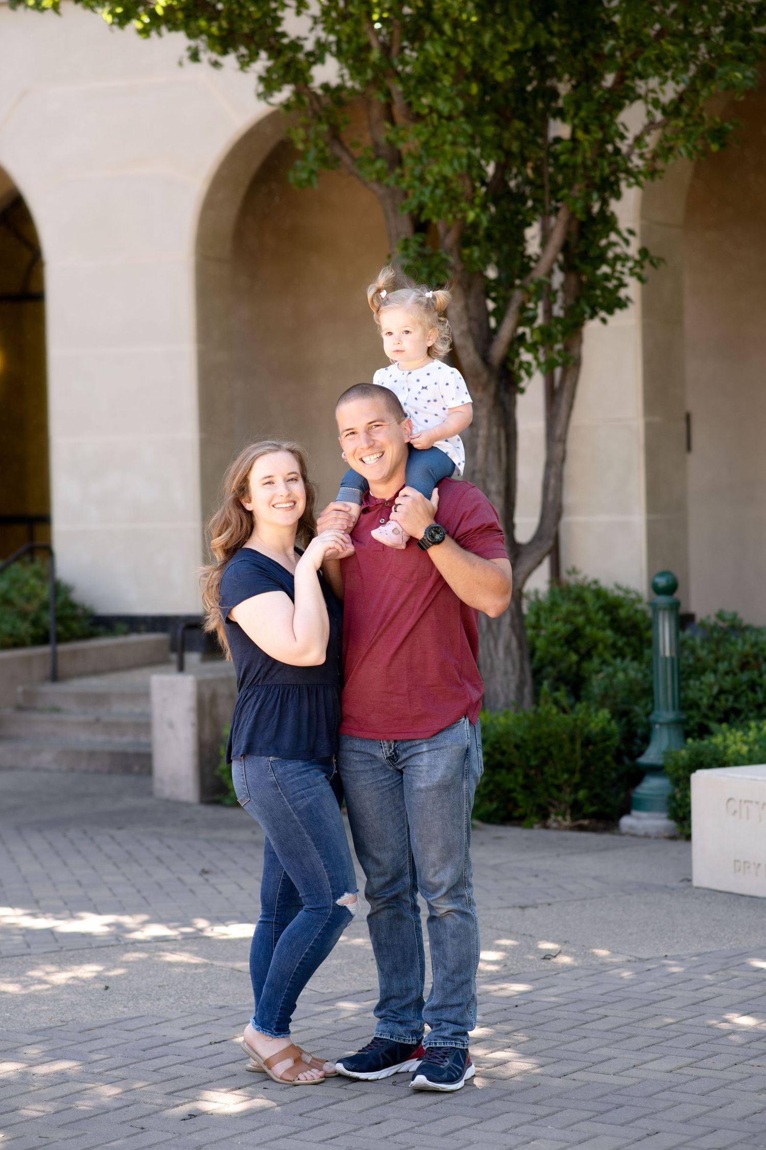 Family portrait taken under a white archway with green foliage in an outdoor courtyard setting.