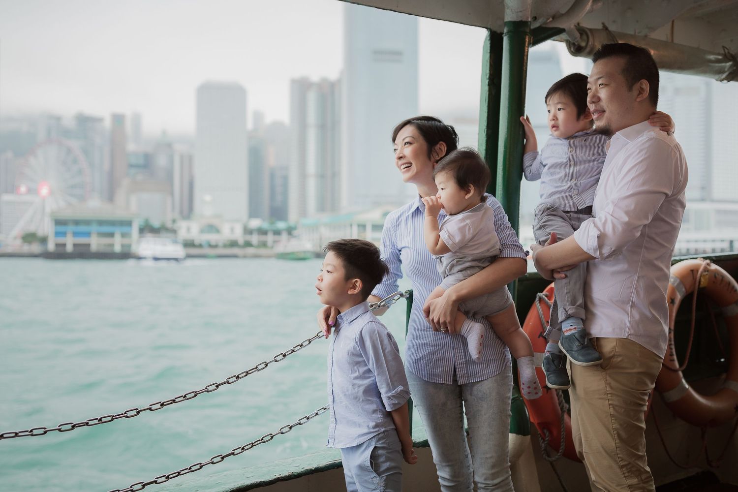 A family enjoys the Hong Kong harbor view from the Star Ferry deck on a sunny day.