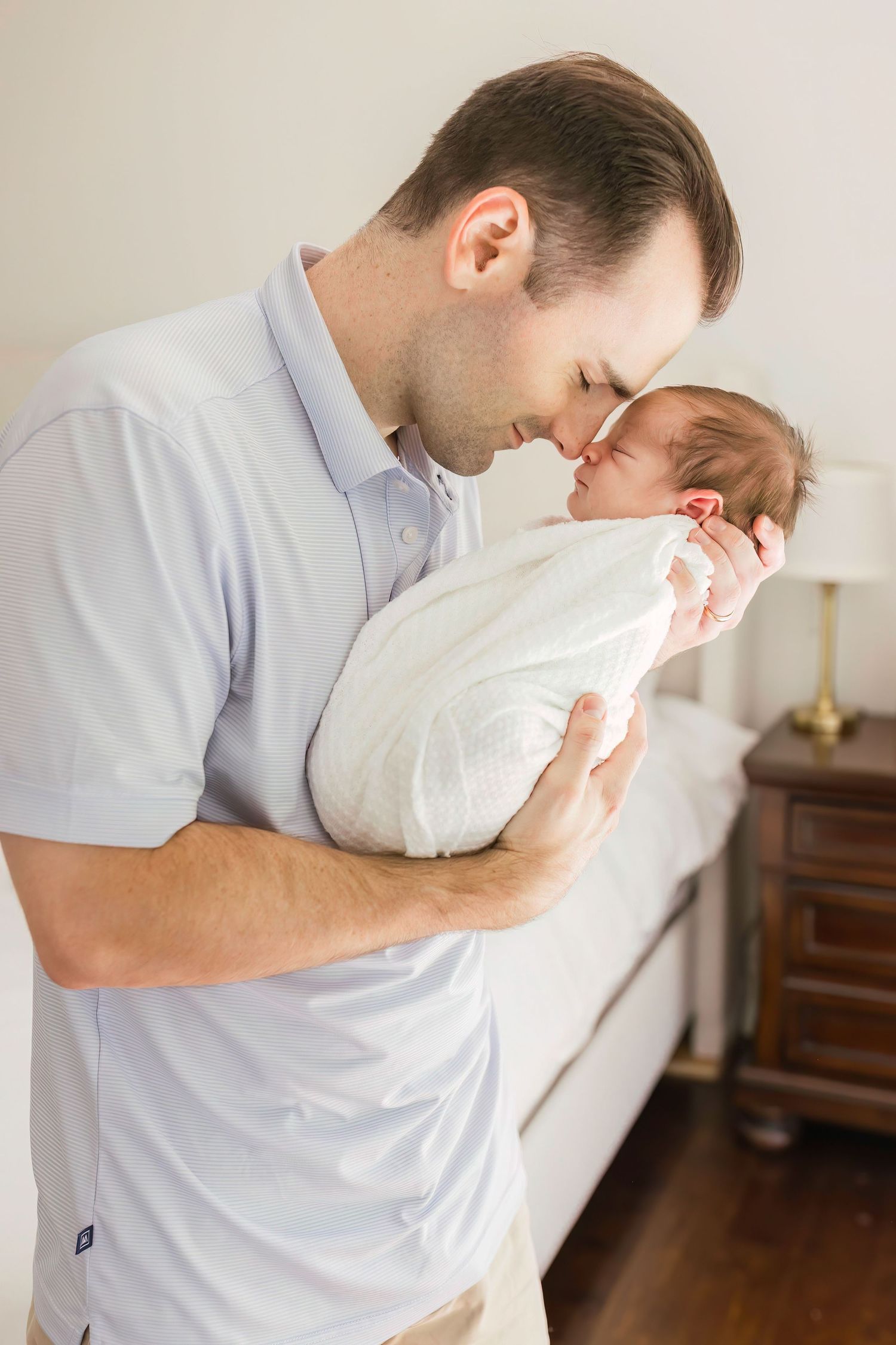 Tender moment between a parent and newborn swaddled in white against a light interior setting.