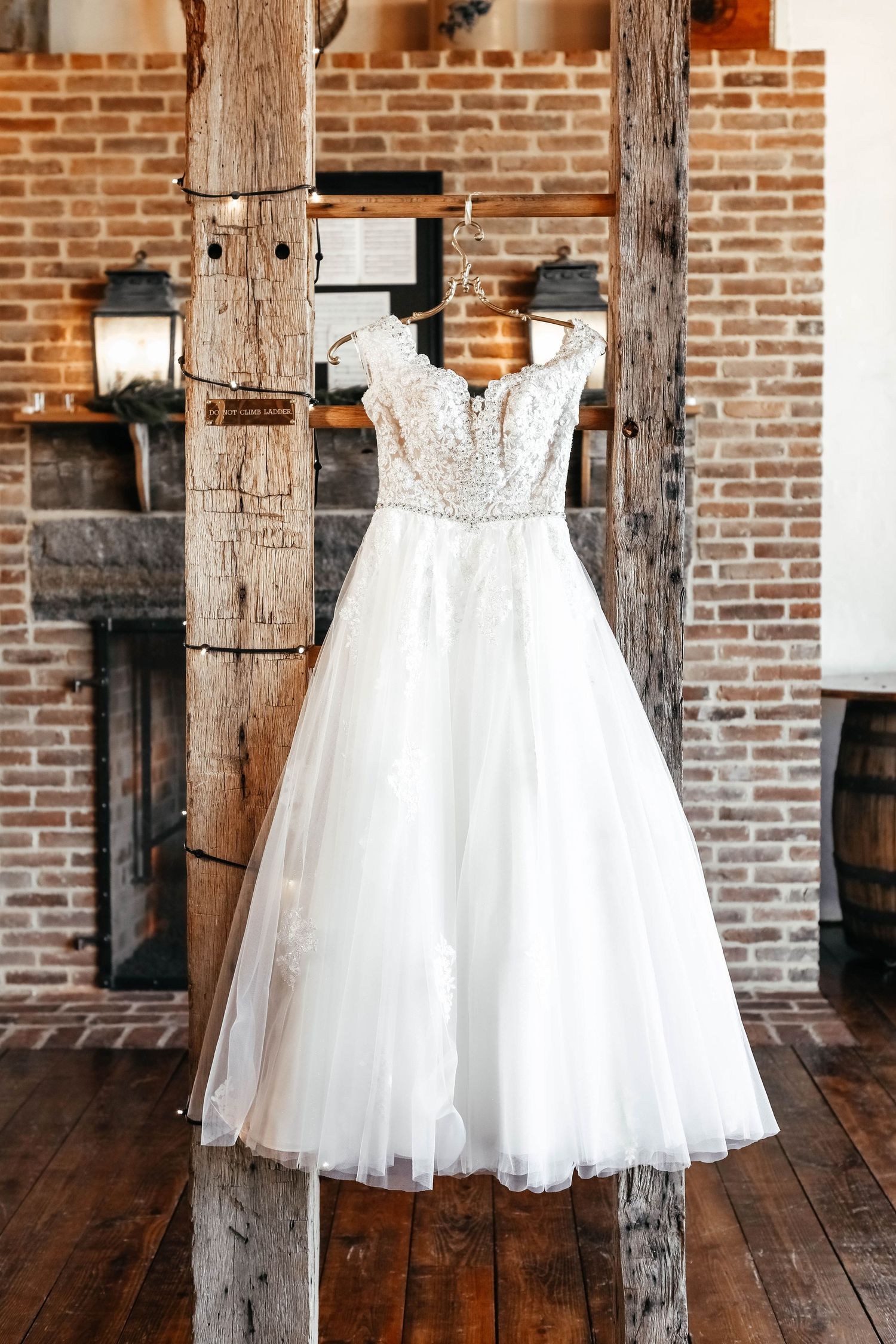 White tulle flower girl dress displayed against rustic wooden beams and brick wall.