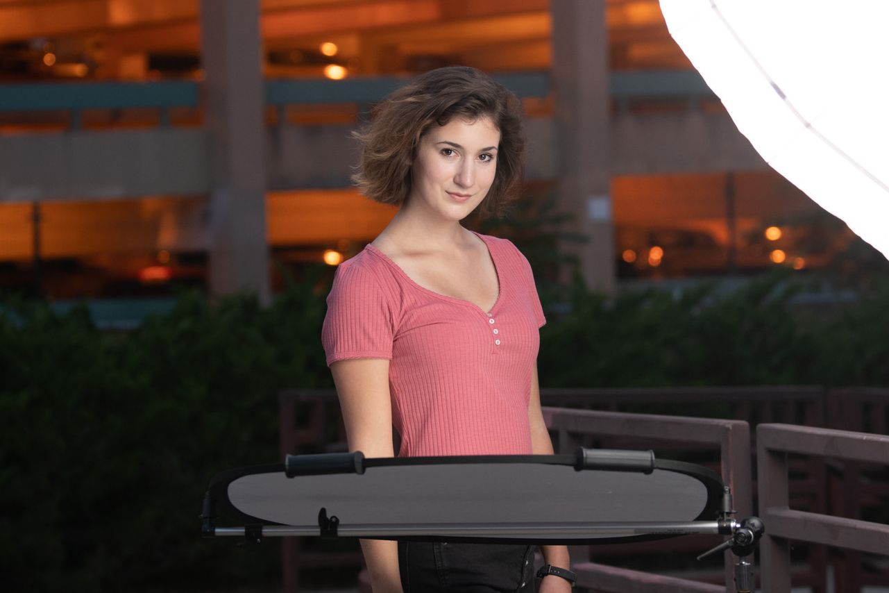 Portrait in a coral top with lighting equipment visible in an outdoor evening setting.