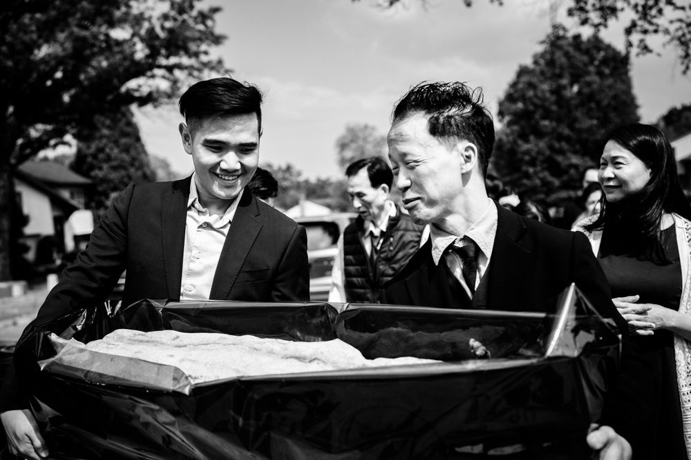 Black and white photo of wedding guests mingling outdoors under trees.