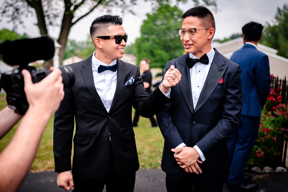Groomsmen in black tuxedos and bowties share laughs during outdoor wedding photos.