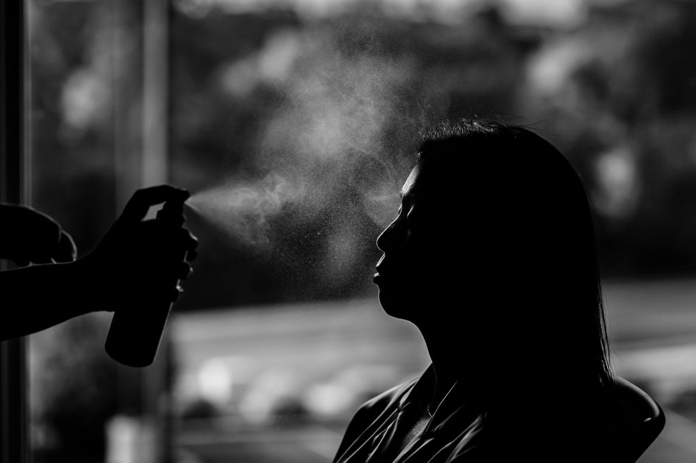 Silhouette of a person getting hair styled with visible spray mist.